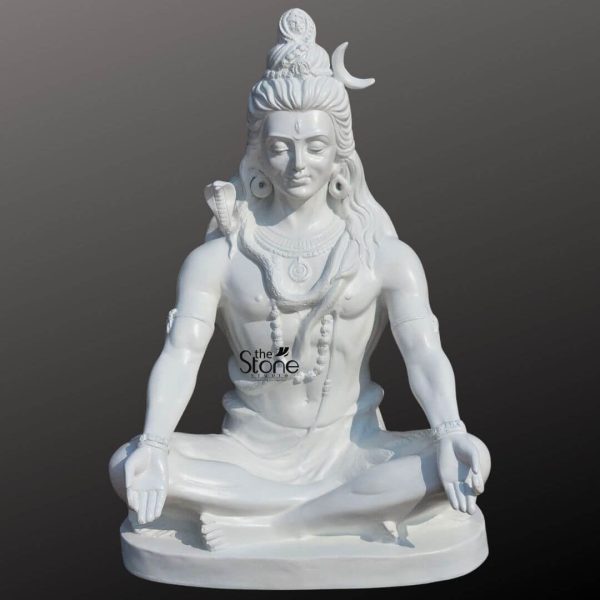 An exquisitely detailed 2-foot tall Lord Shiva meditation statue masterfully hand-carved from premium white material with a smooth, polished finish, perfect for a home mandir or meditation room. The sculpture captures the deity in a profound state of inner peace, seated in the traditional Padmasana atop an oval pedestal. Lord Shiva is depicted with his eyes closed in deep contemplation, featuring a serene and tranquil facial expression. The iconography is rendered with precision, including the towering matted hair adorned with a slender crescent moon on the side and a small, finely carved figure of Goddess Ganga emerging from the top, representing his Gangadhara form. A sacred cobra serpent is gracefully coiled around his neck, and the deity is further embellished with multiple layers of Rudraksha bead necklaces traditional armlets, and wristbands. His hands rest calmly on his knees in the Gyan Mudra the universal gesture of wisdom and mindfulness. This 2ft white Shiva idol radiates an aura of divine protection and spiritual stability, making it an ideal spiritual centerpiece for a contemporary or traditional home sanctuary, designed to invite peace and positive energy into the living space.