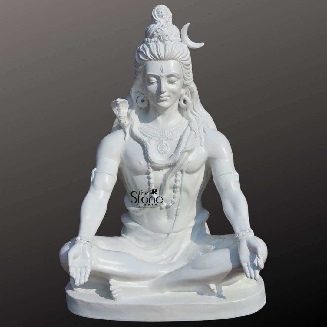 2ft Shiva Meditation Statue 1 An exquisitely detailed 2-foot tall Lord Shiva meditation statue masterfully hand-carved from premium white material with a smooth, polished finish, perfect for a home mandir or meditation room. The sculpture captures the deity in a profound state of inner peace, seated in the traditional Padmasana atop an oval pedestal. Lord Shiva is depicted with his eyes closed in deep contemplation, featuring a serene and tranquil facial expression. The iconography is rendered with precision, including the towering matted hair adorned with a slender crescent moon on the side and a small, finely carved figure of Goddess Ganga emerging from the top, representing his Gangadhara form. A sacred cobra serpent is gracefully coiled around his neck, and the deity is further embellished with multiple layers of Rudraksha bead necklaces traditional armlets, and wristbands. His hands rest calmly on his knees in the Gyan Mudra the universal gesture of wisdom and mindfulness. This 2ft white Shiva idol radiates an aura of divine protection and spiritual stability, making it an ideal spiritual centerpiece for a contemporary or traditional home sanctuary, designed to invite peace and positive energy into the living space.