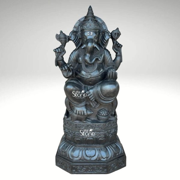 A magnificent 3.5-foot black stone Ganesha statue sits gracefully showcasing intricate craftsmanship perfect for a garden setting. The deity is depicted in a traditional seated posture on a beautifully carved lotus pedestal which rests upon an octagonal base. Ganesha's elephant head features large ears expressive eyes and a prominent trunk curled towards his left. He is adorned with an elaborate crown necklaces and armlets all meticulously sculpted to highlight the fine details of the black stone. In his upper two hands Ganesha holds a conch shell and an axe while his lower right hand is in a gesture of blessing and his lower left hand holds a bowl of modak. The overall finish of the black stone gives the statue a sophisticated and timeless appearance making it a striking centerpiece for any garden or outdoor space. The statue's substantial size and detailed artistry emphasize its grandeur and spiritual significance aligning perfectly with its description as a 3.5ft Ganesha Garden Statue.