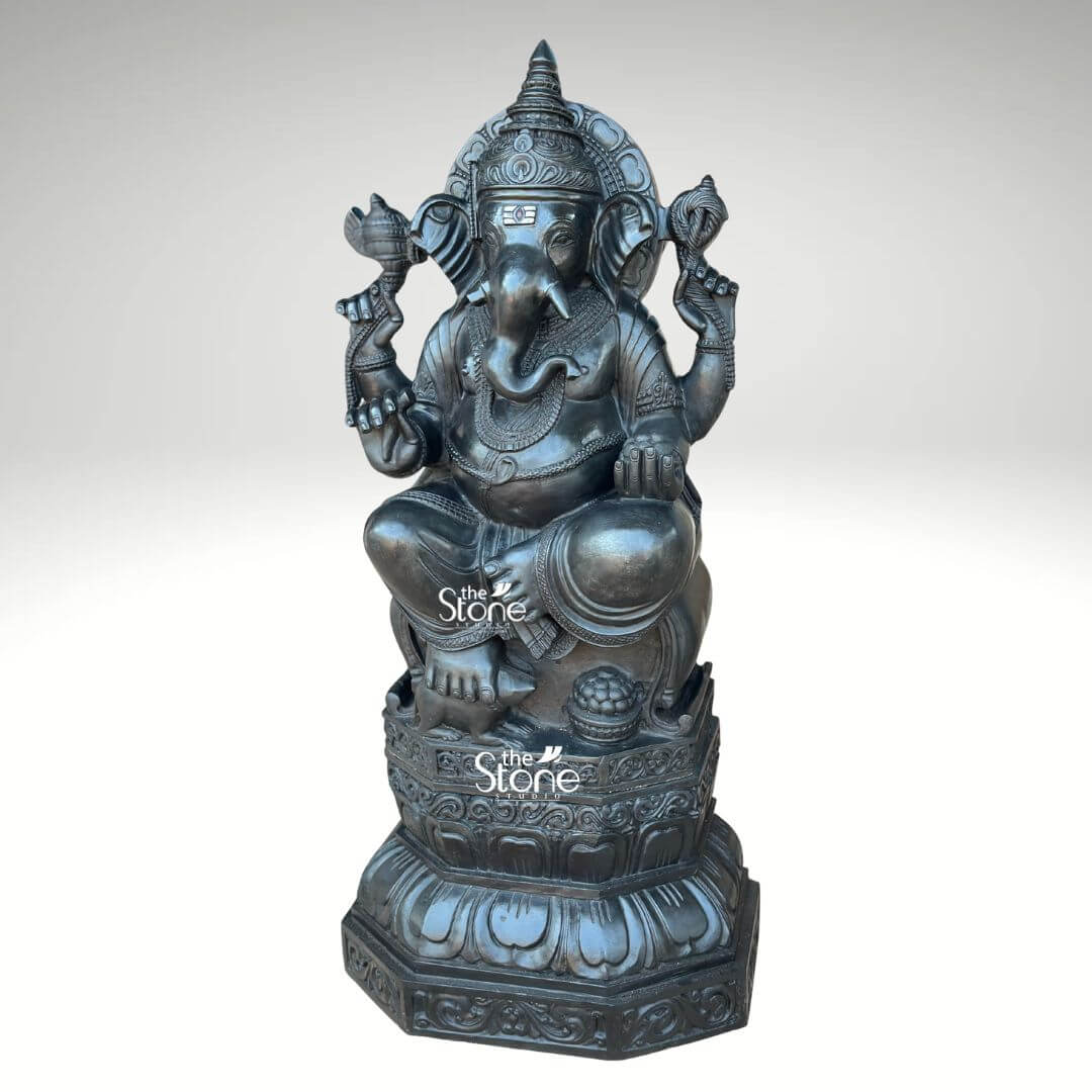 3.5ft Ganesha Garden Statue 6 This image features a magnificent 3.5-foot black stone Ganpati statue presented with a keen focus on its impressive scale and intricate artistry against a clean light background. The deity is depicted in a traditional seated posture radiating a sense of calm and wisdom. Ganesha's iconic elephant head is meticulously sculpted showcasing prominent fanned ears a serene expression in his eyes and a gracefully curved trunk that reaches towards his left symbolizing auspiciousness and the ability to discern. He is adorned with an elaborate crown, intricate necklaces, and finely detailed armlets and anklets, all of which are carved with exceptional precision, enhancing the statue's regal appearance. The statue rests upon a beautifully layered lotus pedestal a classic symbol of purity and spiritual awakening. This pedestal, in turn is supported by a robust octagonal base featuring additional intricate carvings of lotus petals and other decorative motifs that underscore the statue's sacred significance. In his upper right hand, Ganesha holds a conch shell and in his upper left an axe – traditional implements associated with divine sound and the severing of attachments. His lower right hand is extended in a gesture of blessing, offering grace and protection, while his lower left hand cradles a bowl of modak, his favorite sweet symbolizing the rewards of spiritual pursuit. The dark smooth finish of the black stone lends a profound sense of gravitas and timeless elegance to the sculpture making it a powerful and sophisticated representation of Lord Ganesha. The overall craftsmanship and detailed ornamentation of this 3.5ft Ganpati Statue ensure it serves not only as a spiritual artifact but also as a striking piece of art. This alt text emphasizes the visual elements that convey the statue's connection to the article's content, highlighting its suitability as a substantial and aesthetically rich focal point for any setting be it a home, temple or garden.