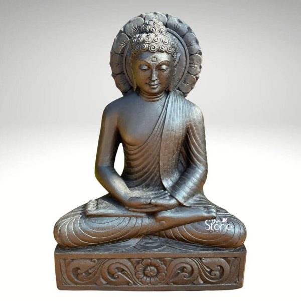 This image features a serene 2-foot Buddha statue masterfully carved from dark black stone, presented against a plain light background that highlights its graceful contours and contemplative presence. This Black Stone Buddha Idol for Garden is depicted in the classic meditative lotus position with his legs crossed and the soles of his feet facing upwards. His hands rest gently in his lap in the Dhyana Mudra palms facing upwards symbolizing deep concentration and spiritual perfection. The Buddha's face conveys profound tranquility, with eyes gently closed or downcast a subtle smile and elongated earlobes that signify his renunciation of worldly possessions. His hair is tightly curled forming an ushnisha the cranial bump representing his enlightened wisdom. A prominent aureole or halo intricately carved with lotus petal motifs, frames his head, symbolizing his divine radiance. The monastic robe drapes elegantly over his left shoulder with fine, flowing lines indicating the delicate fabric and skilled artistry of the carving. The statue rests on a solid, rectangular base, which is also made of black stone and adorned with elegant floral and swirling vine carvings along its front. The dark, rich tone of the stone gives the statue a grounded and timeless quality, making it an ideal piece for outdoor settings. The overall aesthetic of this 2-foot Buddha statue in black stone is one of peace and introspection, designed to bring a sense of calm and spiritual beauty to any garden or outdoor meditation space.