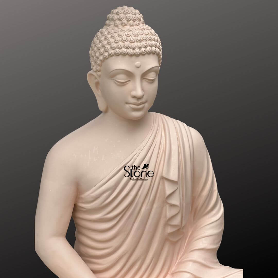 Buddha Statue for Home Decor 4 Feet 4 A serene 4-foot fiber Buddha statue ideal for home Vastu is presented in a close-up slightly elevated shot of its upper body against a plain dark background. The statue is crafted from a light possibly off-white or very pale pink fiber giving it a smooth and calming aesthetic suitable for promoting positive energy according to Vastu principles. Buddha's face exudes profound tranquility, with downcast eyes and a subtle, benevolent smile, embodying deep inner peace and contemplation. A small urna is visible between his brows, symbolizing spiritual insight. His hair is meticulously sculpted in tight, uniform curls topped with an ushnisha symbolizing heightened spiritual wisdom. The flowing robes are rendered with soft graceful folds elegantly draped over his left shoulder and across his body revealing his right shoulder. The smooth finish of the fiber material highlights every delicate detail of his serene form, from the gentle curves of his features to the naturalistic drapery of his robe. This detailed image effectively conveys the spiritual essence and artistic craftsmanship of the fiber Buddha statue, making it highly relevant to an article discussing its use for home Vastu.