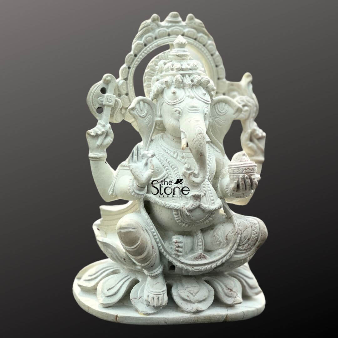 Small Ganesha Idol for Car Dashboard 4" 5 A intricately carved white stone Ganesha statue perfectly sized for a car dashboard is showcased against a plain dark background. Lord Ganesha is depicted in a traditional seated posture on a multi-petaled lotus base exuding an aura of peace and prosperity. He possesses four arms his upper right hand holds an axe or goad, while his upper left hand grasps a noose (partially visible). His lower right hand is raised in a gesture of blessing (Abhaya Mudra), and his lower left hand gently holds a small bowl filled with modaks towards which his trunk gracefully curves. The white stone material beautifully highlights the fine details of his crown, elaborate jewelry and the folds of his dhoti. A decorative halo or prabhavali with a detailed outer edge frames Ganesha's head, emphasizing his divine presence. The smooth texture and precise carvings make this Ganesha idol a compact yet powerful symbol. This detailed image clearly conveys the artistry and spiritual significance of the white stone Ganesha idol, making it highly relevant to an article on car dashboard placement.