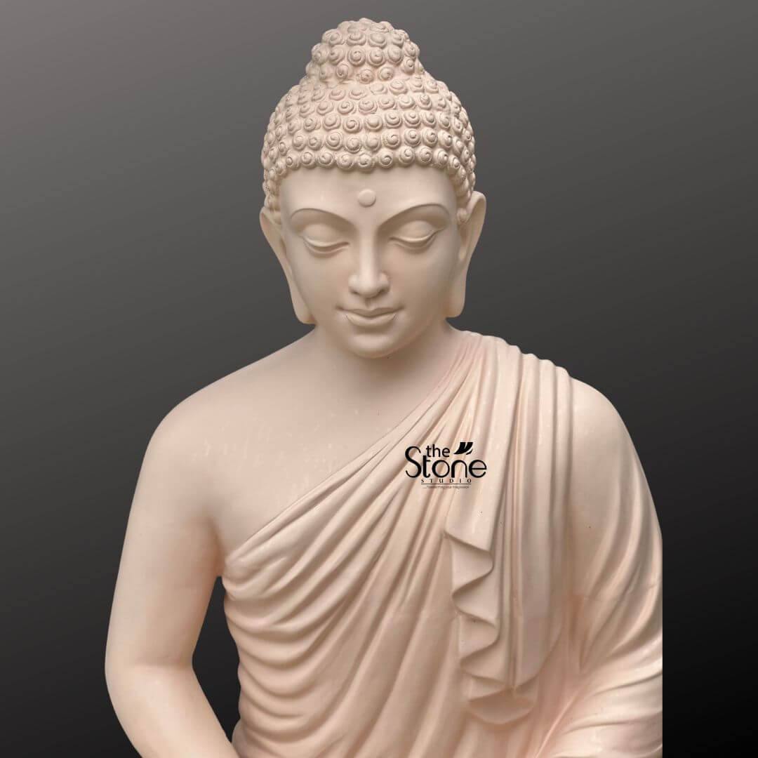 Buddha Statue for Home Decor 4 Feet 6 A close-up slightly elevated shot captures the upper body of a serene 4-foot fiber Buddha statue ideal for terrace decor set against a plain dark background. The statue is crafted from a light, possibly off-white or very pale pink fiber giving it a smooth and calming aesthetic suitable for an outdoor meditative space. Buddha's face exudes profound tranquility, with gently closed or downcast eyes and a subtle benevolent smile embodying deep inner peace and contemplation. A small urna is visible between his brows, symbolizing spiritual insight. His hair is meticulously sculpted in tight uniform curls, topped with an ushnisha symbolizing heightened spiritual wisdom. The flowing robes are rendered with soft graceful folds elegantly draped over his left shoulder and across his body revealing his right shoulder. The smooth finish of the fiber material highlights every delicate detail of his serene form from the gentle curves of his features to the naturalistic drapery of his robe. This detailed image effectively conveys the spiritual essence and artistic craftsmanship of the fiber Buddha statue, making it highly relevant to an article discussing its use for terrace decor.