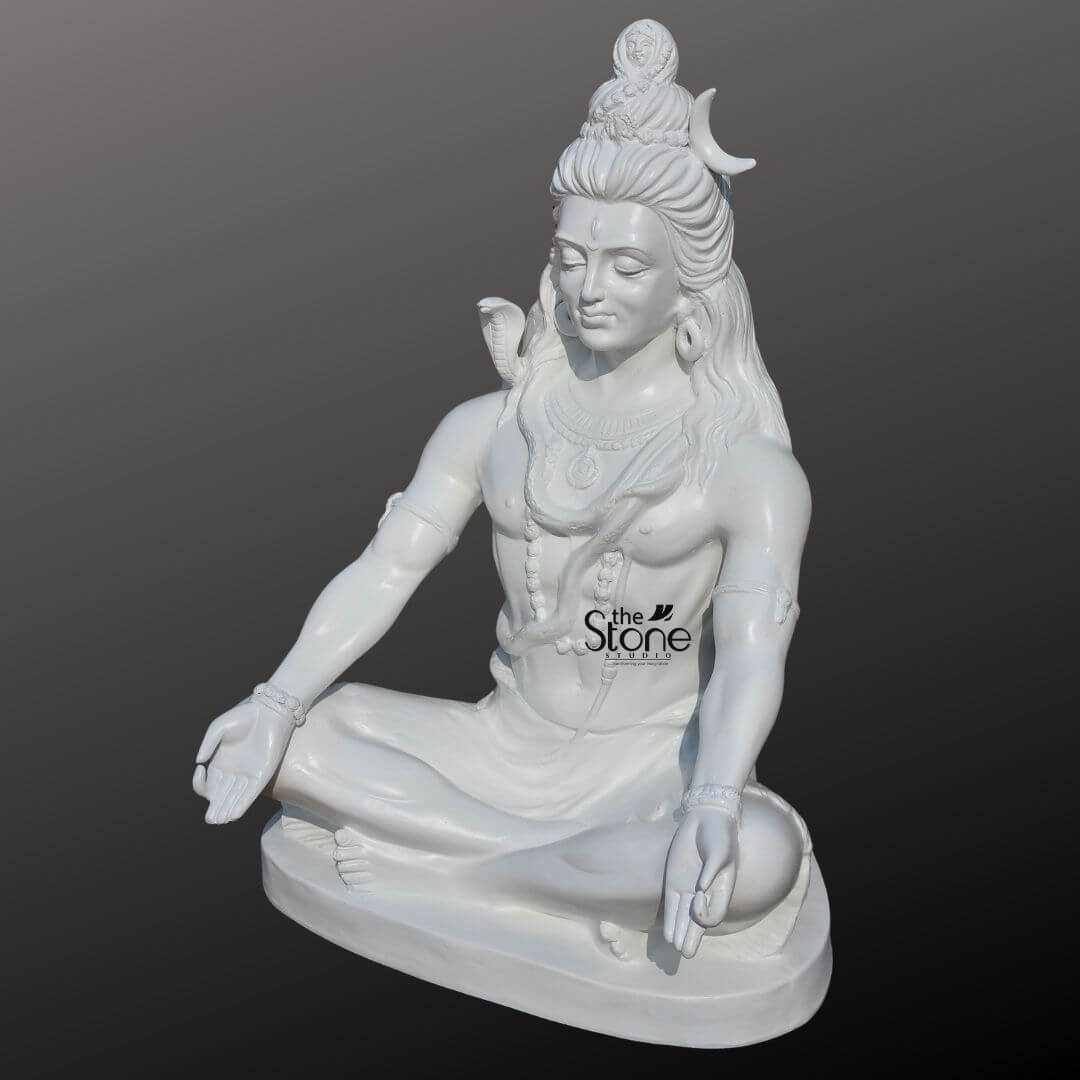 2ft Shiva Meditation Statue 2 An expertly handcrafted 2-foot tall Lord Shiva statue for home masterfully sculpted from premium white material with a smooth, polished finish that mimics the elegance of white marble. Shown from a three-quarter side perspective to emphasize its depth, the deity is depicted in a serene meditative posture seated cross-legged on a solid, stable base. The sculpture features intricate traditional iconography: his high matted hair (Jata) holds a slender white crescent moon and a small, finely carved figure of Goddess Ganga emerging from the top. A sacred cobra serpent is gracefully coiled around his neck, and he is further adorned with realistic Rudraksha bead necklaces traditional armlets, and bracelets. Lord Shiva's hands rest calmly on his knees in the Gyan Mudra of wisdom and peace. This 2ft white Shiva idol radiates an aura of profound tranquility and divine protection, making it a perfect spiritual centerpiece for a home mandir meditation sanctuary, or personal altar.