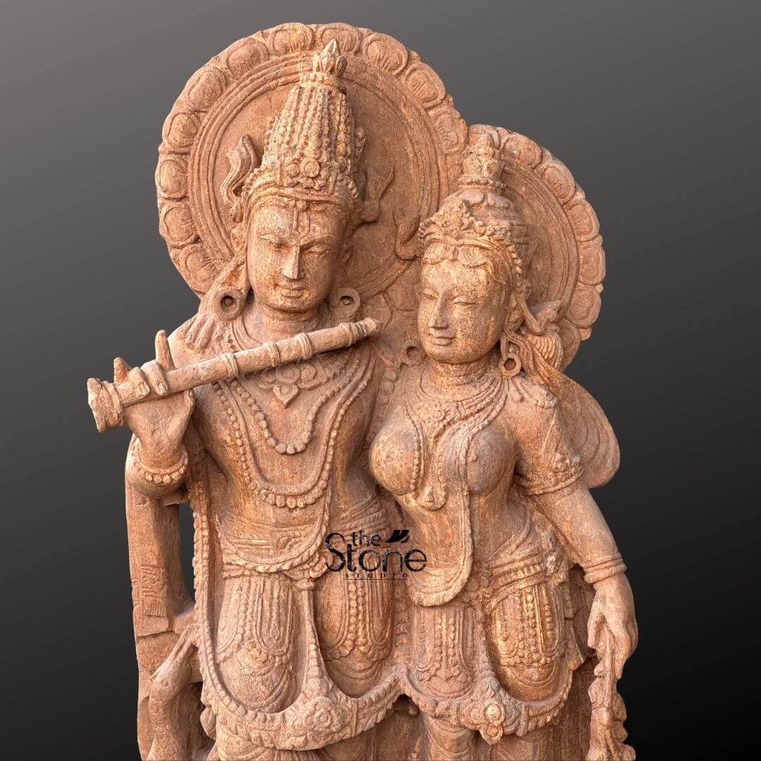 Radha Krishna Sandstone Garden Statue 3ft 2 An exquisitely hand-carved Radha Krishna sandstone statue masterfully sculpted from natural brown stone with a rich grainy texture. This detailed upper body shot captures the divine couple Lord Krishna and Goddess Radha in a state of spiritual harmony. Krishna is shown in his iconic flute-playing pose wearing a towering tiered crown and layered necklaces while a grand circular halo frames his head. Standing elegantly beside him Goddess Radha is depicted with a gentle compassionate expression adorned with traditional jewelry and an intricately carved sari. The sculpture showcases exceptional artisan detail in the realistic fabric-like folds of their attire and the rhythmic floral patterns on their haloes. The warm earthy reddish-brown tones of the natural sandstone provide a timeless, antique aesthetic illustrating how a handcrafted stone Radha Krishna idol can serve as a profound spiritual focal point for home mandir or garden decor.