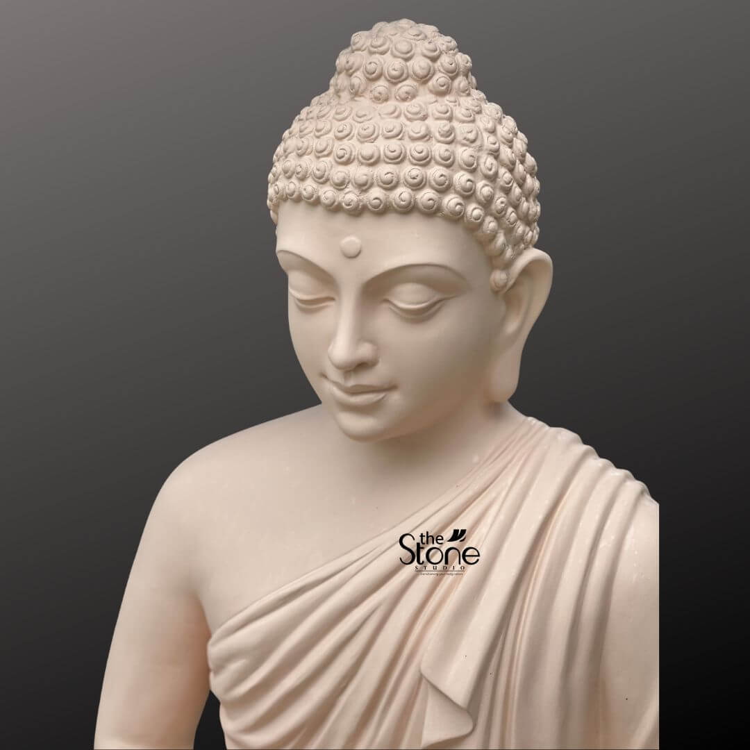 Buddha Statue for Home Decor 4 Feet 7 A serene close-up view of the upper torso and head of a 4-foot tall Lord Buddha idol masterfully designed as a majestic spiritual centerpiece for a large indoor space. The large Buddha statue is crafted from high-quality durable fibre material with a soft matte finish that beautifully mimics the refined texture of natural stone. The deity is captured in a state of profound peace and deep meditation, featuring a tranquil facial expression with eyes gently closed and a subtle, compassionate smile. Masterful artisan detailing is evident in the traditional ushnisha—the small, tight curls of hair gathered at the crown—and the elongated earlobes that symbolize divine wisdom. The monastic robe is draped elegantly over the left shoulder showcasing realistic and fluidly carved fabric folds that add a sense of grace and three-dimensional depth to the sculpture. This large-scale fibre Buddha sculpture is a perfect choice for an indoor home mandir a grand foyer or a dedicated meditation room inviting an atmosphere of mindfulness, tranquility, and sophisticated spiritual decor into the living environment.