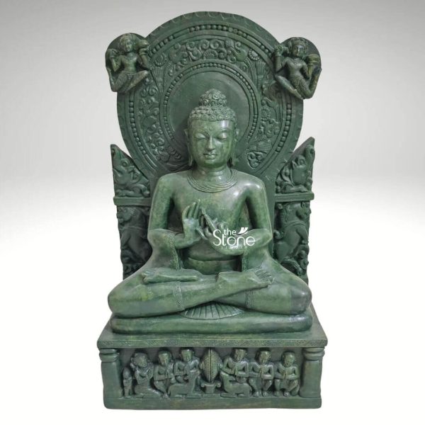 A majestic 2-foot tall Lord Buddha meditation statue masterfully handcarved from natural green stone serves as a profound spiritual centerpiece for a home mandir or Zen garden. The sculpture depicts the Buddha in a serene seated Padmasana atop an intricately detailed rectangular pedestal featuring high-relief carvings of several smaller figures likely disciples in devotional poses. Lord Buddha’s hands are held in the sacred Dharmachakra Mudra the universal gesture of teaching and the turning of the wheel of dharma. The deity is framed by a grand circular Prabhavali embellished with traditional rhythmic patterns and celestial figures carved into the upper corners. The deep emerald green hue and polished finish of the green stone Buddha highlight the exceptional artisan craftsmanship from the peaceful facial expression and elongated earlobes to the traditional ushnisha. This large scale stone sculpture is designed to invite an aura of deep peace mindfulness and divine wisdom into any interior or exterior landscape, perfectly illustrating the timeless beauty of traditional Indian stone art.