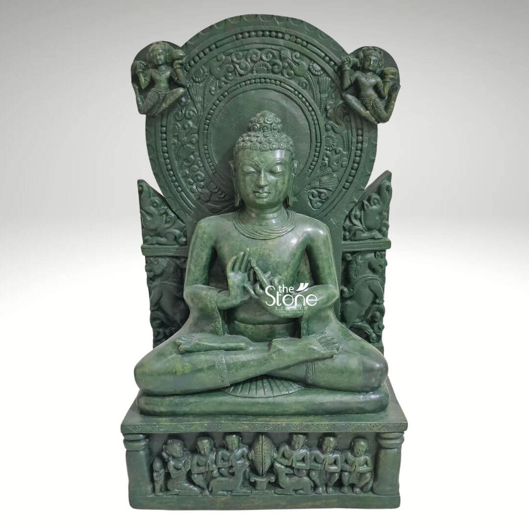 Meditation Buddha Statue 2ft 1 A majestic 2-foot tall Lord Buddha meditation statue masterfully handcarved from natural green stone serves as a profound spiritual centerpiece for a home mandir or Zen garden. The sculpture depicts the Buddha in a serene seated Padmasana atop an intricately detailed rectangular pedestal featuring high-relief carvings of several smaller figures likely disciples in devotional poses. Lord Buddha’s hands are held in the sacred Dharmachakra Mudra the universal gesture of teaching and the turning of the wheel of dharma. The deity is framed by a grand circular Prabhavali embellished with traditional rhythmic patterns and celestial figures carved into the upper corners. The deep emerald green hue and polished finish of the green stone Buddha highlight the exceptional artisan craftsmanship from the peaceful facial expression and elongated earlobes to the traditional ushnisha. This large scale stone sculpture is designed to invite an aura of deep peace mindfulness and divine wisdom into any interior or exterior landscape, perfectly illustrating the timeless beauty of traditional Indian stone art.