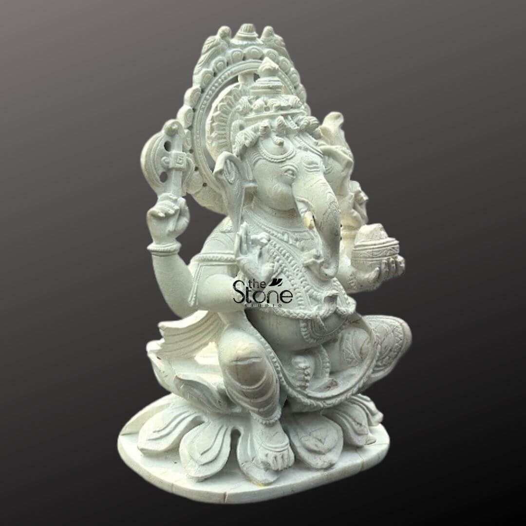 Small Ganesha Idol for Car Dashboard 4" 6 A meticulously carved white stone Ganesha statue presented as a mini Ganpati murti suitable for a car dashboard is captured against a plain dark background. The statue depicts Lord Ganesha in a traditional seated slightly squatting posture on a multi-layered lotus base symbolizing purity and growth. He is portrayed with four arms; his upper right hand holds an axe or goad, while his upper left hand holds a noose (partially visible). His lower right hand is raised in a gesture of blessing and his lower left hand holds a small bowl of modaks with his trunk curving towards it indicating his love for sweets. The pristine white stone material beautifully accentuates the intricate details of his crown elaborate jewelry and the folds of his dhoti. A decorative halo or prabhavali with a serrated outer edge frames Ganesha's head enhancing his divine presence. The smooth texture and fine artistry of the carving make this Ganesha idol a compact and auspicious item. This detailed image clearly illustrates the sacred and decorative qualities of the white stone Ganesha statue making it highly relevant to an article discussing car dashboard placement.