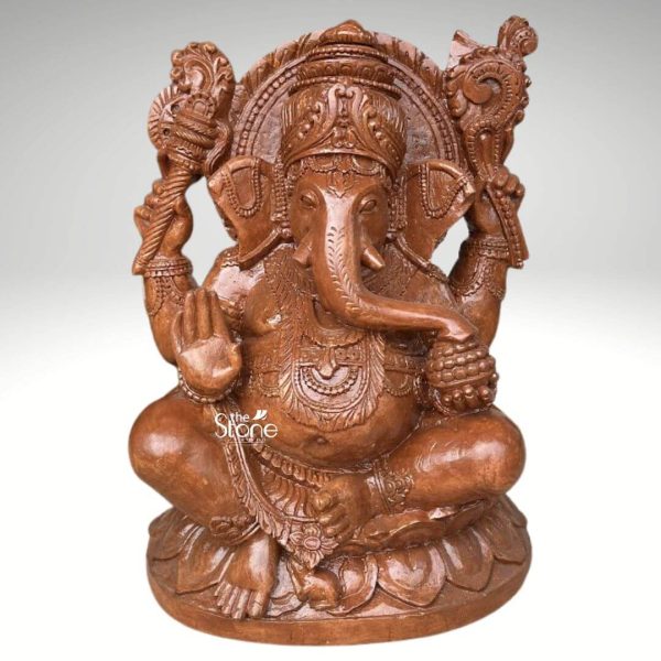 An exquisitely hand-carved 2.5-foot tall Lord Ganesha statue also known as Pillaiyar masterfully sculpted from premium natural brown sandstone. This large-scale spiritual masterpiece depicts the deity in an auspicious and stable seated posture atop an intricately detailed multi-tiered lotus pedestal which symbolizes purity and spiritual grounding. Lord Ganesha is portrayed with his iconic elephant head featuring a serene facial expression a gracefully curved trunk, and large ears that represent the wisdom of listening. The deity has four arms carrying sacred Vedic symbols: his upper hands hold the pasha and ankusha to guide and remove obstacles while his lower right hand is raised in the Abhaya Mudra the universal gesture of protection and blessing. The craftsmanship highlights incredible artisan detail from the towering tiered mukut and layered necklaces to the armlets and realistic fabric folds of his traditional attire. At the base of the statue the small figure of his loyal vehicle, the mouse is subtly carved. The refined matte finish and grainy, earthy reddish-brown texture of the sandstone highlight the heritage of traditional Indian stone masonry, making this 30-inch Ganesha idol a perfect addition to invite peace prosperity and divine stability into a home mandir, grand foyer, or garden landscape.