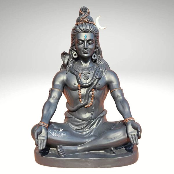A serene 2-foot Shiv Shankar statue crafted from dark fiber material depicts Lord Shiva in a classic meditative pose. He is seated cross-legged with his hands resting gently in his lap palms open embodying deep contemplation and peace. Shiva's eyes are closed suggesting profound meditation and a prominent blue third eye is visible on his forehead symbolizing wisdom and insight. His long, matted hair is styled into a topknot adorned with a crescent moon and a small cobra iconic symbols of Shiva. Another cobra is intricately wrapped around his neck serving as a necklace and a mala prayer bead necklace is draped across his chest. He wears simple armbands and bracelets further emphasizing his ascetic nature. The dark, smooth finish of the fiber material gives the statue a contemporary yet timeless aesthetic. The muscular yet calm physique of Shiva is finely detailed showcasing the artistry of the sculpture. The statue is placed on a simple, round base reinforcing its stability and elegant presentation. This sculpture perfectly captures the essence of Lord Shiva as a yogi and the ultimate reality, making it a compelling piece for any devotee or collector.