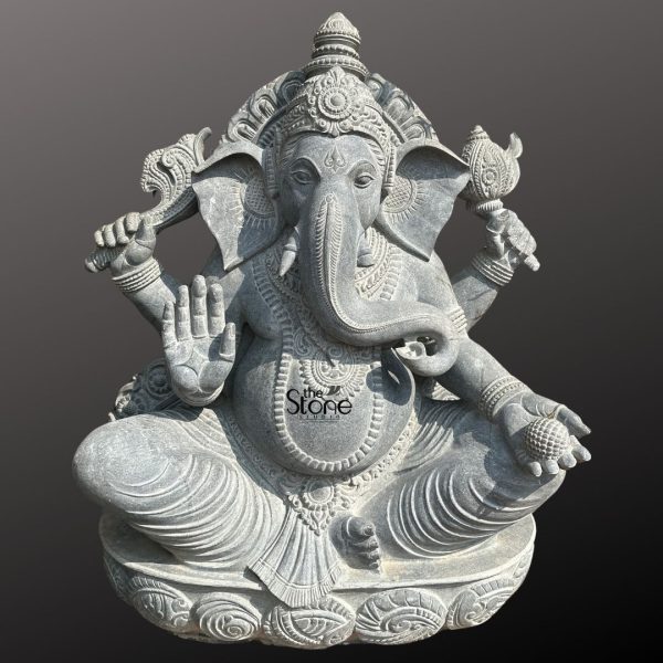 An exquisitely hand-carved 4-foot tall Sri Vinayaka statue made from premium natural blackstone serving as a majestic spiritual centerpiece for a home mandir, grand foyer, or garden landscape. This large-scale black stone Ganesha statue depicts the deity in an auspicious and stable seated posture atop an intricate, multi-tiered lotus pedestal embellished with detailed relief carvings. Lord Ganesha is portrayed with four arms carrying sacred spiritual symbols: his upper hands hold a traditional axe and goad to guide and remove obstacles, while his lower right hand is raised in the Abhaya Mudra the universal gesture of protection and blessing. His trunk curves gracefully toward a large modak (traditional sweet) held in his lower left hand representing the sweetness of spiritual attainment. The craftsmanship showcases incredible detail, from the towering, tiered mukut and large expressive fan-like ears to the layered necklaces, armlets, and realistic fabric folds of his traditional attire. The refined matte charcoal finish of the stone highlights the heritage of traditional Indian stone masonry making this 4ft Sri Vinayaka idol a perfect addition to any space to invite peace, prosperity, and the removal of obstacles.