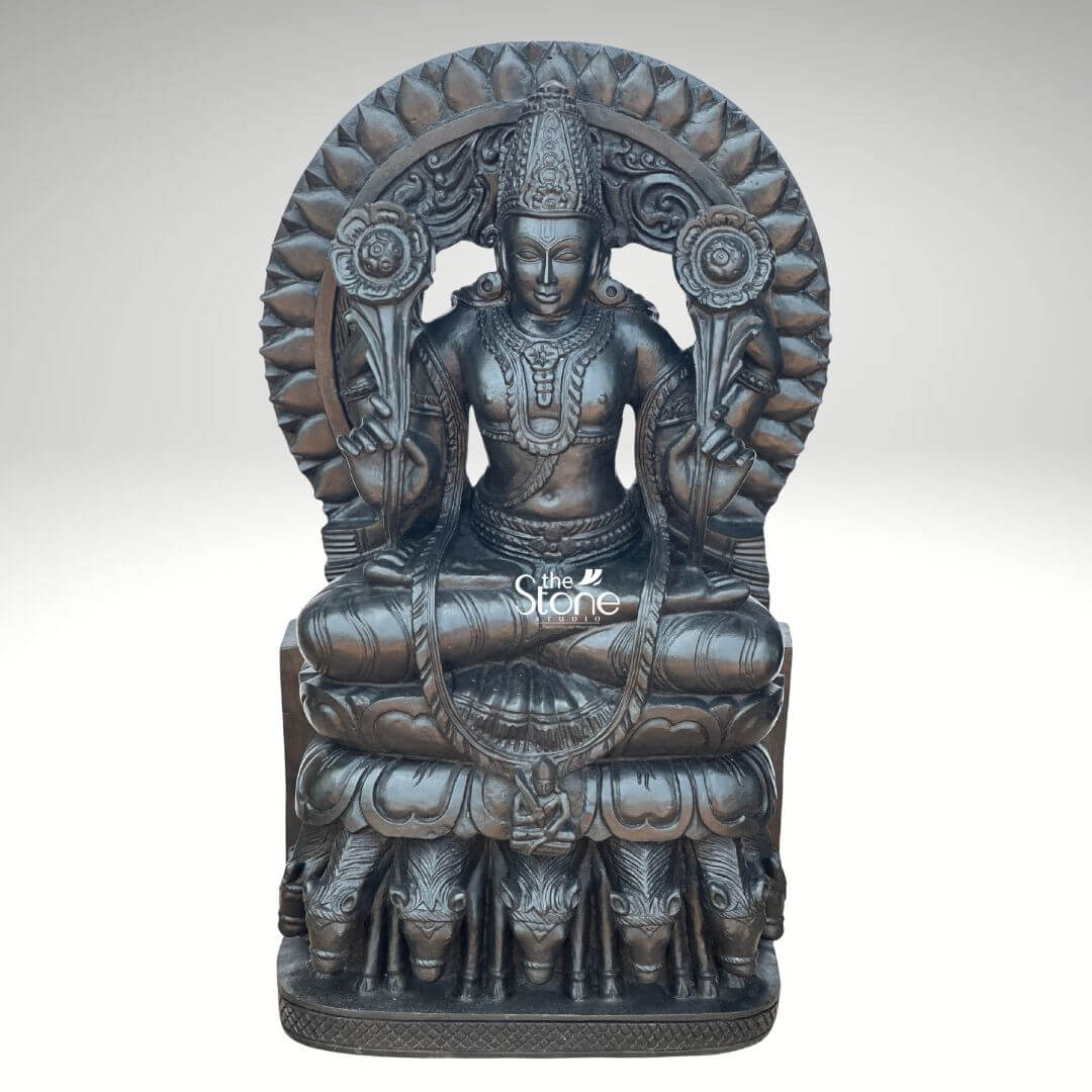 Surya Dev Black Stone Statue 30" 1 A majestic 2.5-feet black stone Surya Dev statue is presented from a frontal slightly elevated perspective against a plain light background. The sculpture depicts Surya Dev the Hindu solar deity seated in a regal posture embodying power and enlightenment. The entire statue is meticulously carved from rich dark black stone which gives it a profound and traditional presence, with a subtle, antique-like sheen. Surya Dev is shown with two arms each holding a blooming lotus flower symbols of purity and creation. He is richly adorned with an elaborate crown intricate necklaces armlets, earrings and a sacred thread across his chest. His serene face with slightly downcast eyes radiates benevolence. Behind his head rises a grand, circular prabhavali intricately carved with lotus petals radiating outwards symbolizing the sun's rays and his divine effulgence. The most distinctive feature of the statue is its base: Surya Dev is seated atop a chariot driven by seven horses, which are exquisitely carved in a row beneath his lotus throne representing the seven colors of the rainbow or the seven days of the week. The smooth yet detailed finish of the black stone highlights the fine artistry and the powerful benevolent presence of the solar deity. This detailed image powerfully conveys the spiritual majesty and artistic craftsmanship of the black stone Surya Dev statue, making it highly relevant to an article discussing such revered idols.