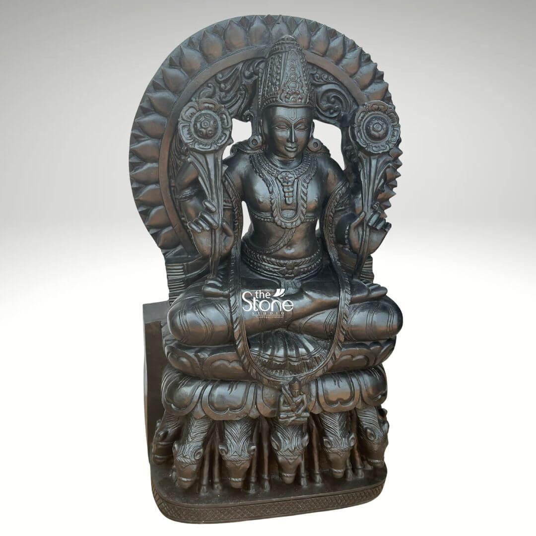 Surya Dev Black Stone Statue 30" 9 An exquisitely hand-carved 2.5-foot tall Surya God statue with seven horses masterfully sculpted from premium natural black stone with a refined matte charcoal finish. This spiritual masterpiece depicts the Sun God in a traditional seated posture atop a majestic, multi-tiered pedestal, radiating an aura of divine energy and cosmic power. Lord Surya is portrayed with two arms each holding a long-stemmed, blooming lotus flower, symbolizing purity and the awakening of consciousness. Framing the head and upper body is a grand, circular Prabhavali embellished with rhythmic, petal-like relief patterns that represent the life-giving rays of the sun. A defining iconographic feature of this black stone Surya Dev statue is the seven horses carved in high relief at the base of his celestial chariot representing the seven days of the week and the seven colors of light. This durable and weather-resistant 30-inch stone sculpture serves as a profound spiritual icon, ideal for a home mandir, grand foyer, or office space, designed to invite vitality, success, and positive energy into the surroundings.