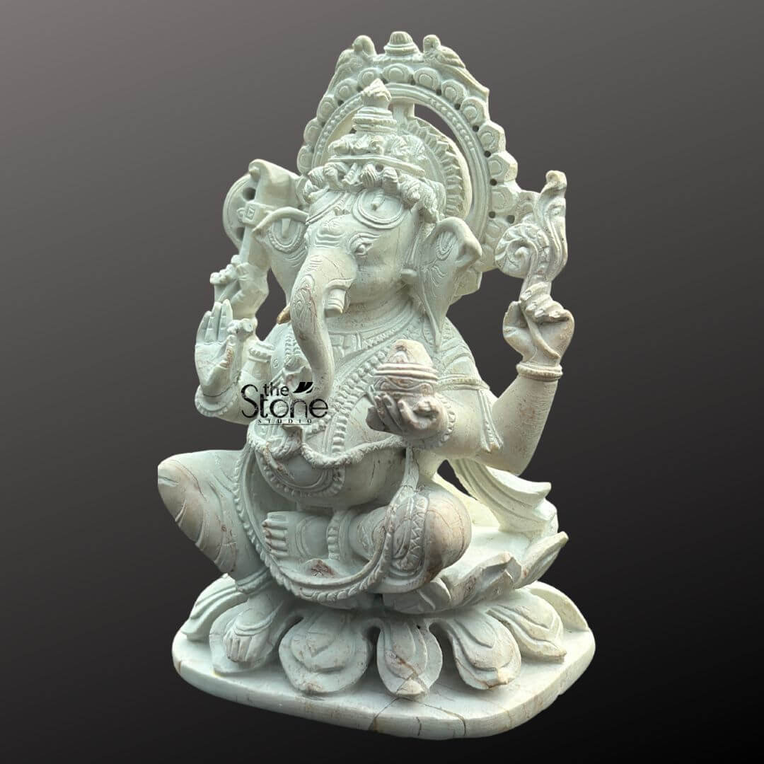 Small Ganesha Idol for Car Dashboard 4" 4 An exquisite white stone Ganesha statue presented as an ideal Ganpati idol for a car dashboard is captured against a plain dark background. The statue depicts Lord Ganesha in a traditional seated posture on an intricately carved lotus base symbolizing purity and spiritual awakening. He is portrayed with four arms his upper right hand holds an axe or goad while his upper left hand holds a noose (partially visible). His lower right hand is raised in a gesture of blessing and his lower left hand gently holds a small bowl brimming with modaks towards which his trunk gracefully curves. The pristine white stone material beautifully accentuates the fine details of his ornate crown elaborate jewelry and the flowing drapery of his dhoti. A decorative halo or prabhavali, with a serrated outer edge and possibly additional carvings within, frames Ganesha's head, enhancing his divine presence. The smooth finish and precise artistry of the carving make this Ganesha idol a compact yet powerful symbol. This detailed image clearly illustrates the sacred and decorative qualities of the white stone Ganesha statue making it highly relevant to an article discussing car dashboard placement.