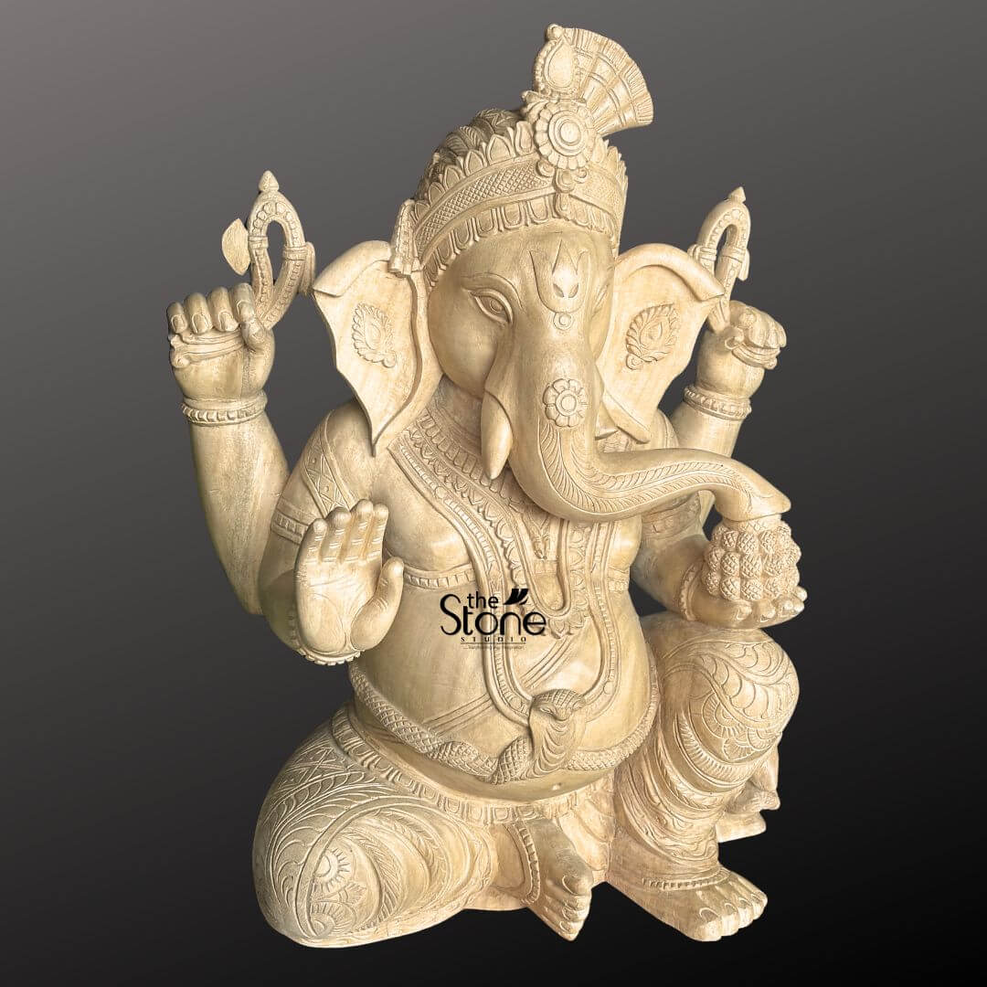 Wooden Ganesha Statue Online 2ft 7 A masterfully hand-carved 2-foot tall wooden Ganesha statue perfectly designed as an auspicious centerpiece for a home temple or mandir. Sculpted from natural light-toned wood with a smooth polished finish, this Ganpati idol is shown in a majestic seated posture radiating a sense of peace and stability. Lord Ganesha is portrayed with four arms carrying traditional spiritual symbols: his upper hands hold a carved goad and a noose to guide and remove obstacles while his lower right hand is raised in the Abhaya Mudra the universal gesture of protection and blessing. His trunk curves gracefully toward a bowl of modaks held in his lower left hand, symbolizing the rewards of a spiritual life. The sculpture features exceptionally intricate detailing, from the towering, tiered mukut to the layered necklaces, armlets, and realistic, fluid fabric folds of his traditional dhoti. At the base of the statue, the small figure of his loyal vehicle, the mouse is delicately carved near his foot. This 24-inch wooden Ganesha sculpture represents the peak of traditional Indian artisan craftsmanship, making it an ideal choice for a wooden temple Ganesha idol designed to invite wisdom, prosperity, and divine energy into any living space.