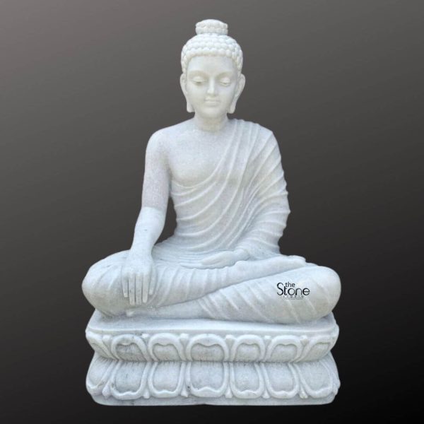A magnificent three-foot marble Buddha idol is elegantly presented against a dark neutral background highlighting its pristine white material and serene form. This statue ideal for an article about a large marble Buddha idol depicts the Buddha seated in a meditative lotus position emanating an aura of profound peace enlightenment and spiritual tranquility. His right hand rests gently on his knee in the Bhumisparsha Mudra symbolizing his moment of enlightenment under the Bodhi tree while his left hand rests in his lap palm facing upwards. The craftsmanship of the statue is exceptional showcasing the smooth luminous white marble that exquisitely captures the delicate details of the Buddha's form. His robes are gracefully draped over his body with naturalistic flowing pleats that add depth and realism without detracting from the overall serene aesthetic. The Buddha's facial features are finely sculpted with a calm and contemplative expression characteristic of traditional Buddhist art. A prominent ushnisha on his head symbolizes wisdom and spiritual attainment while his hair is meticulously carved into tight symmetrical curls. His elongated earlobes are indicative of his princely past and renunciation of worldly possessions. The Buddha is seated upon a beautifully carved lotus pedestal also made from white marble. This pedestal features multiple layers of intricately detailed lotus petals symbolizing purity spiritual awakening and beauty. The pristine white marble reflects light softly giving the statue a luminous quality that enhances its divine presence. This three-foot marble Buddha idol is not just a work of art but a powerful spiritual artifact suitable for a temple meditation center or a prominent place in a home inspiring devotion and providing a focal point for spiritual practice and inner peace.