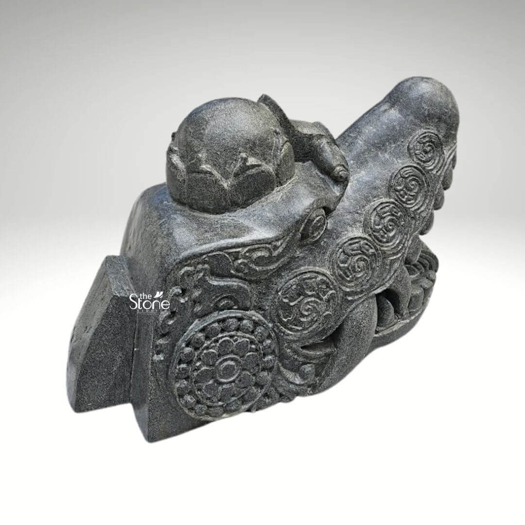 Dragon Head Statue 18" 8 A detailed black stone dragon head sculpture measuring 1.5 feet in length and 1 foot in height is expertly carved and displayed against a plain light background. This formidable statue serves as a striking example of traditional artistry and the powerful symbolism of dragons making it an excellent subject for an article on dragon head sculptures. The dragon's head is rendered with a robust snout and a wide-open mouth revealing menacing stylized fangs and a meticulously textured interior conveying an impression of immense power ancient wisdom and protective vigilance. The rich dark black stone material gives the sculpture a profound and timeless quality emphasizing its strength and durability. The entire surface of the dragon's head is adorned with an array of intricate traditional carvings. These include flowing swirling patterns that skillfully mimic the complex texture of scales and suggest dynamic movement along with prominent circular motifs. These circular designs reminiscent of ancient symbols or stylized floral elements are strategically integrated into the overall ornamentation adding significant cultural depth and artistic elegance to the piece. The eyes are deeply set and carved with a piercing watchful gaze which enhances the sculpture's commanding and mystical demeanor. A distinctive crown-like or horn-like protrusion on the top of the head further accentuates its majestic and mythical status reinforcing its symbolic power. The craftsmanship is exemplary showcasing varied textures across the sculpture from the smoother more refined areas to the rugged detailed scales and ridges along the jawline and brow. This intricate play of textures creates a dynamic visual effect allowing light and shadow to highlight the three-dimensional form and bring the mythical creature to vivid life. This blackstone dragon head sculpture is more than just a decorative item it serves as a powerful cultural and artistic artifact, embodying strength good fortune and protection. Its substantial size and material make it suitable for a prominent display in various settings such as a garden an entrance or a collector's showcase, as implied by its general description as a dragon head sculpture.