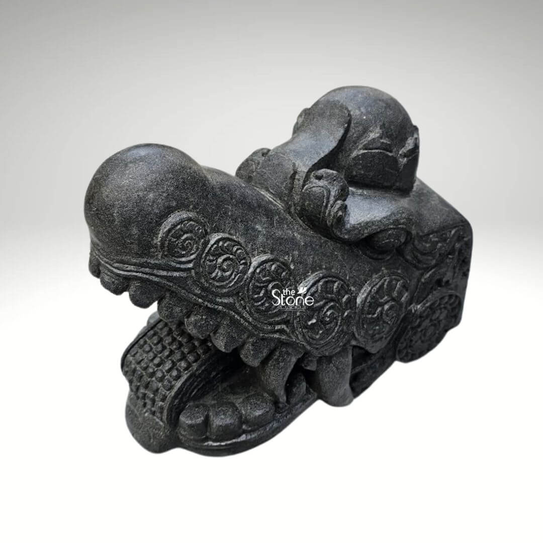 Dragon Head Statue 18" 4 A captivating black stone dragon head statue meticulously carved to measure 1.5 feet in length and 1 foot in height is displayed against a clean plain background. This intricately detailed sculpture is an ideal artistic and symbolic element for a home entrance designed to invoke protection and grandeur. The dragon's head is depicted with an open powerful snout revealing formidable fangs and a textured mouth interior conveying a sense of alertness and guardianship. The dark rich black stone material gives the sculpture an ancient and robust quality ensuring its resilience and timeless appeal for both indoor and outdoor settings. The surface of the dragon's head is adorned with elaborate swirling patterns and intricate circular motifs which are characteristic of traditional dragon art. These carvings wrap around the head suggesting scales and imparting a sense of mystical energy and movement. The eyes are deeply set and carved with a piercing gaze enhancing the dragon's watchful and protective demeanor. A distinctive crown-like or horn-like protrusion on the top of the head further elevates its majestic and mythical status reinforcing its symbolic power. The craftsmanship is evident in the varied textures across the sculpture from the smoother polished areas to the more rugged detailed scales and ridges along the jawline and brow. This interplay of textures creates a dynamic visual effect allowing light and shadow to highlight the three dimensional form and bring the mythical creature to life. This blackstone dragon head statue is not just a decorative piece it serves as a powerful cultural statement symbolizing strength good fortune and protection making it a perfect addition to a home entrance to ward off negative energies and welcome prosperity as discussed in an article about such traditional home embellishments.