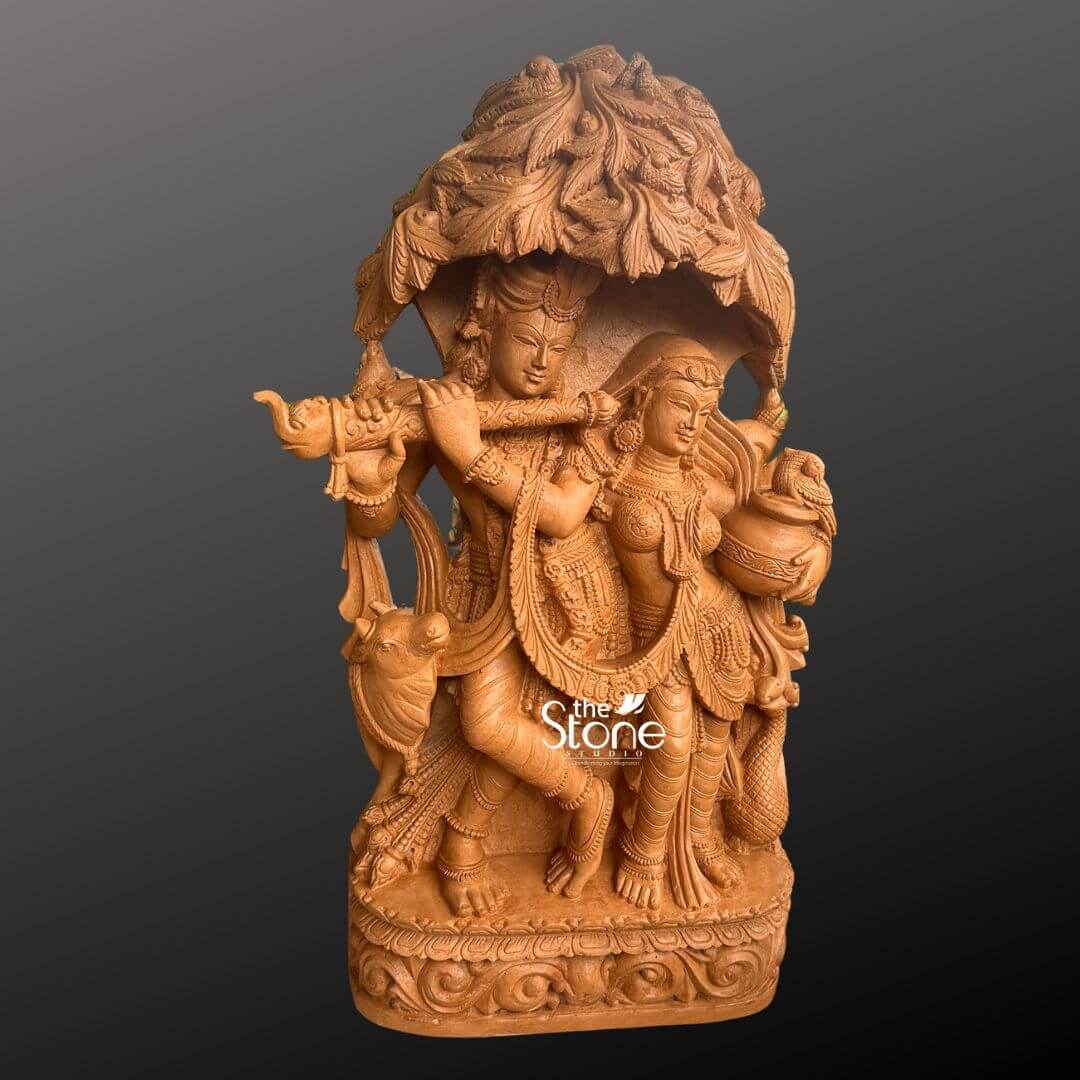 Radha Krishna Idol for Garden Décor 3.5ft 6 A magnificent 3.5-foot Radha Krishna idol meticulously carved from rich brown sandstone, is prominently displayed against a deep dark grey background making it an exquisite piece for home décor. The divine couple Radha and Krishna are depicted standing gracefully together under an elaborate intricately sculpted tree canopy with Lord Krishna captivating Radha with his flute. Lord Krishna stands on the left, holding a flute to his lips his expression one of divine charm and musical enchantment. He is adorned with an ornate crown multiple necklaces armlets, and flowing dhoti all rendered with exceptional detail in the brown sandstone. A sacred cow a symbol closely associated with Krishna is intricately carved near his feet adding a pastoral and traditional element to the scene. Radha stands gracefully beside him on the right her face expressing deep devotion and enchantment holding a pot or pitcher symbolizing offerings or the abundance of nature. She is also beautifully adorned with a crown necklaces, and a flowing sari, with all drapery and jewelry finely sculpted. The most striking feature is the dense overarching tree canopy above them meticulously carved with numerous leaves and branches in high relief from the same brown sandstone providing a naturalistic and sacred shelter. The entire 3.5-foot Radha Krishna statue rests on a sturdy multi-tiered rectangular base which is richly decorated with traditional scrolling and floral motifs along its edges. The warm earthy tone and subtle texture of the brown sandstone give the sculpture a natural timeless, and elegant aesthetic, perfectly blending with various home décor styles. This detailed brown sandstone sculpture beautifully embodies eternal love devotion, and harmony, directly aligning with an article discussing Radha Krishna idols in sandstone for home décor.