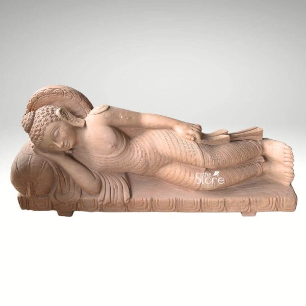 A serene 4.5-foot Reclining Buddha statue crafted from sandstone is elegantly displayed against a soft plain white background highlighting its suitability for garden decor. The statue depicts Buddha in the Mahaparinirvana pose lying on his right side with his head gently resting on a pillow conveying a profound sense of peace tranquility and ultimate enlightenment. The sandstone material gives the statue a natural earthy reddish-brown hue with a smooth slightly textured finish that hints at its natural origin. The Buddha's form is gracefully sculpted with flowing robes that drape subtly over his body indicated by delicate incised lines suggesting soft fabric. His facial features are rendered with exquisite calm eyes gently closed a serene smile and elongated earlobes characteristic of Buddha imagery. Tightly curled hair covers his head and a prominent urna is visible on his forehead. Behind his head a beautifully carved halo or aura emanates symbolizing his divine wisdom and enlightenment. The entire figure rests on an elongated rectangular base that also features carved details including a lotus petal motif along the lower edge providing a stable and aesthetically pleasing foundation. The statue's substantial size and natural stone finish make it an ideal weather-resistant feature for a garden meditation space or any outdoor area seeking to evoke a sense of calm spirituality and timeless beauty.