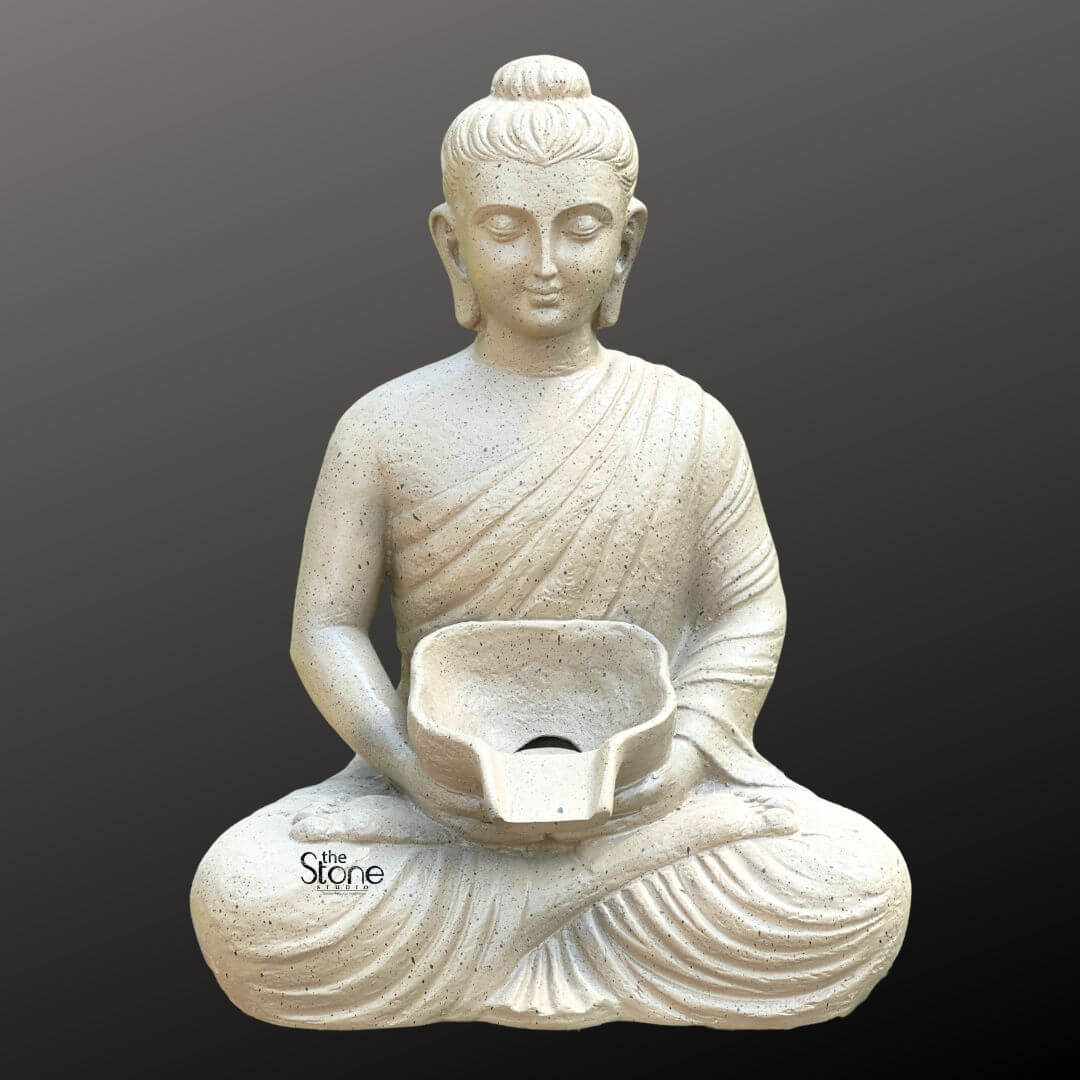 Wall-Mounted Buddha Fountain 3ft 6 A tranquil wall-mounted Buddha fountain crafted from fiber with a textured light gray finish is presented against a dark minimalist background emphasizing its serene aesthetic and functional design. This sculpture features the Buddha figure seated in the lotus position emanating a profound sense of peace and meditation. His hands are gently positioned in his lap holding a small shallow bowl that is designed to channel water making it the focal point of a soothing water feature. The Buddha's eyes are softly downcast conveying a deep state of inner calm and spiritual contemplation. The Buddha statue is sculpted with smooth flowing robes draped elegantly over his body, with visible naturalistic folds that add depth and realism to the lightweight fiber material. His facial features are finely rendered and serene featuring a prominent ushnisha on his head symbolizing wisdom and enlightenment and elongated earlobes indicative of his renunciation of worldly possessions. The light neutral color of the fiber speckled with subtle darker flecks mimics the appearance of natural stone lending the statue a timeless and versatile appeal suitable for various decor styles whether indoor or outdoor. The small bowl held in the Buddha's lap has a distinct opening at the front through which water would flow signifying the source of the fountain's gentle cascade. Although the collecting basin is not visible in this specific image the design clearly indicates this piece is the upper component of a wall-mounted fountain system. This fiber Buddha fountain is an ideal piece for creating a calming and meditative atmosphere in any space offering both visual tranquility and the soothing sound of flowing water as highlighted in an article discussing wall-mounted Buddha fountains made of fiber.