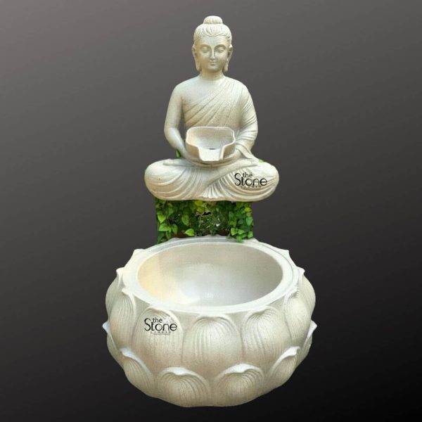 A serene wall-mounted Buddha fountain crafted from fiber and designed to create a peaceful water feature is presented against a dark featureless background highlighting its elegant form. The fountain features a tranquil Buddha figure seated in the lotus position atop a textured green-foliage-like base which implies natural growth or moss. The Buddha's posture is one of deep meditation with hands gently placed in his lap holding a small bowl from which water would gently flow. His eyes are downcast conveying a sense of inner peace and contemplation. The Buddha statue rendered in a light off-white or cream color exhibits smooth flowing robes draped elegantly over his body. His facial features are serene and finely sculpted with a ushnisha on his head symbolizing wisdom and elongated earlobes indicative of his renunciation of worldly possessions. The fiber material allows for a detailed and lightweight construction making it suitable for wall mounting. Below the Buddha figure a large, intricately carved lotus shaped basin collects the water. The basin is also in a similar light color and features multiple layers of detailed lotus petals symbolizing purity and spiritual awakening. The design suggests that water would cascade from the Buddha's bowl into this larger basin, creating a gentle soothing sound. The green foliage beneath the Buddha statue visually connects the upper and lower parts of the fountain adding an organic touch. This Buddha fountain is an ideal piece for creating a calming and meditative atmosphere in a garden, patio or indoor spiritual space as suggested by its use in an article about wall-mounted Buddha fountains.