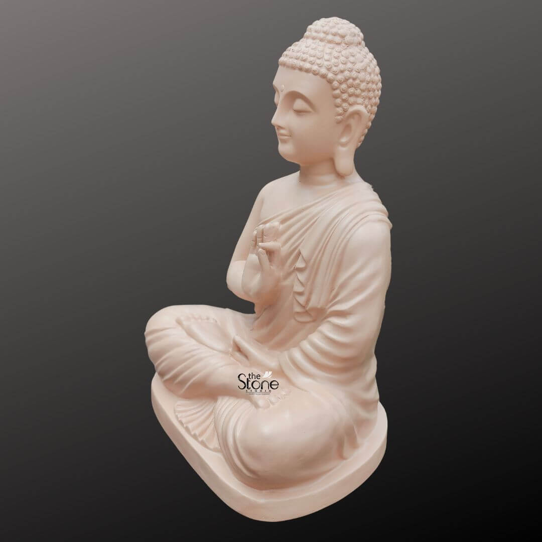 Buddha Statue for Zen Decor 2ft 4 A serene 2-foot fiber Buddha idol, with a smooth, light beige finish, is elegantly presented in a three-quarter side view against a dark, gradient background, making it an ideal centerpiece for a meditation room. The Buddha is depicted in the Vitarka Mudra, with his right hand raised near his chest, palm outward, and thumb and index finger touching to form a circle, symbolizing the teaching and transmission of Buddhist doctrines and encouraging intellectual discussion. His left hand rests gently in his lap, palms upward. Seated in full lotus position, his eyes are gently closed, conveying profound inner peace and spiritual wisdom, while a subtle smile graces his lips, and his elongated earlobes are visible, all characteristic features of traditional Buddha iconography. The detailing on the idol is meticulously rendered, from the individual curls of his hair gathered in a prominent topknot (ushnisha) to the graceful, natural folds of his monastic robe that drape softly over his left shoulder and body. The smooth, matte finish of the fiber material gives the statue a natural, stone-like appearance, perfectly aligning with the calm and uncluttered aesthetics often desired in a meditation space. The light beige color evokes a sense of purity and serenity, enhancing its contemplative presence and making it conducive to quiet reflection. The fiber construction ensures that the statue is robust yet lighter than traditional stone, offering both aesthetic appeal and practical versatility. The Buddha idol rests on a simple, low, and subtly curved rectangular base, which seamlessly integrates with the overall form, providing stability without distracting from the main figure. This 2-foot fiber Buddha idol, with its elegant finish and peaceful demeanor, embodies tranquility and spiritual grace, serving as a captivating subject for an article exploring aesthetically pleasing and durable Buddha statues suitable for enhancing the serene and meditative ambiance of any meditation room.