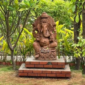 A magnificent 4-foot Ganesha statue crafted from sandstone with a warm reddish-brown hue is proudly situated outdoors on a two-tiered brick platform amidst a lush natural garden setting. Lord Ganesha is depicted in a regal seated posture exuding an aura of wisdom benevolence and auspiciousness. The earthy tone of the sandstone harmonizes beautifully with the surrounding greenery and natural light giving the statue a timeless and grounded presence. The intricate details of Ganesha's elephant head large ears multiple arms and elaborate ornamentation are expertly carved highlighting the artisan's skill. Ganesha is shown with four arms holding traditional attributes such as a conch shell and a disc in his upper hands symbolizing divine power and protection. One of his lower hands holds his broken tusk and the other holds a modak representing wisdom and the sweetness of moksha. A beautifully carved halo or prabhamandala frames his head featuring intricate traditional motifs that enhance his divine aura. The statue sits on a finely sculpted lotus pedestal which in turn rests on a robust rectangular base adding layers of intricate detail. The brick platform itself provides a stable and aesthetically pleasing foundation raising the deity to prominence within the garden. This image is ideally suited for an article discussing 4-foot Ganesha statues particularly for outdoor placement in cities like Pune where such grand figures are highly revered. The substantial size and durable sandstone material make it an impressive and lasting addition to any garden courtyard or temple entrance. The statue's traditional design and its integration into the natural environment showcase its versatility and timeless appeal as a powerful symbol of good fortune success and spiritual harmony deeply connecting with cultural and religious practices.