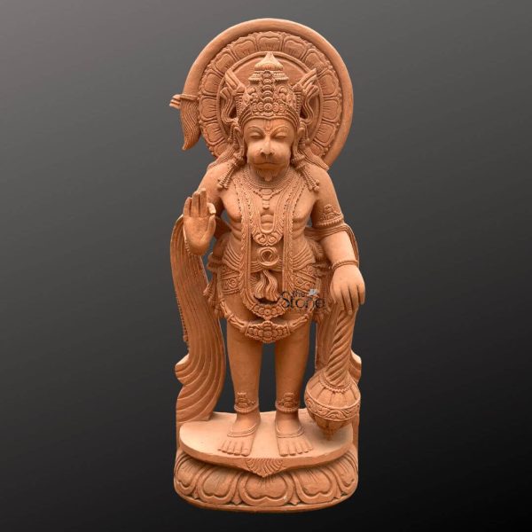 A commanding 4-foot Lord Hanuman Murti expertly carved from rich reddish-brown sandstone stands majestically against a neutral dark background, emphasizing its intricate details and powerful presence. This 4 Feet Hanuman Sandstone statue depicts Hanuman the revered monkey-god in a standing posture radiating strength and devotion. His right hand is raised in the abhaya mudra a gesture of fearlessness and protection while his left hand rests on a massive gada symbolizing his immense power and service. The vibrant color of the sandstone gives the sculpture a warm, earthy appeal suitable for various spiritual and decorative settings. Hanuman is adorned with elaborate traditional attire and ornamentation all meticulously sculpted in the sandstone. He wears a regal crown intricate necklaces armbands and a dhoti with flowing drapery subtly suggested by the carving. His face, with its distinct features characteristic of Hanuman conveys a serene yet determined expression. Behind his head a beautifully carved halo or aureole adds to his divine aura, featuring detailed patterns that highlight the artistry involved in creating this Lord Hanuman Murti. The texture of the sandstone is evident throughout adding depth and authenticity to the figure. The statue stands firmly on a multi-tiered lotus-petal shaped base which is also intricately carved from sandstone providing a stable and aesthetically pleasing foundation. The entire composition emphasizes Hanuman's iconic attributes and his significance as a symbol of strength devotion, and courage making it an ideal visual representation for an article focusing on a 4ft Lord Hanuman Murti. This detailed depiction not only showcases the artistic skill but also the spiritual essence embodied in a large-scale sandstone deity.