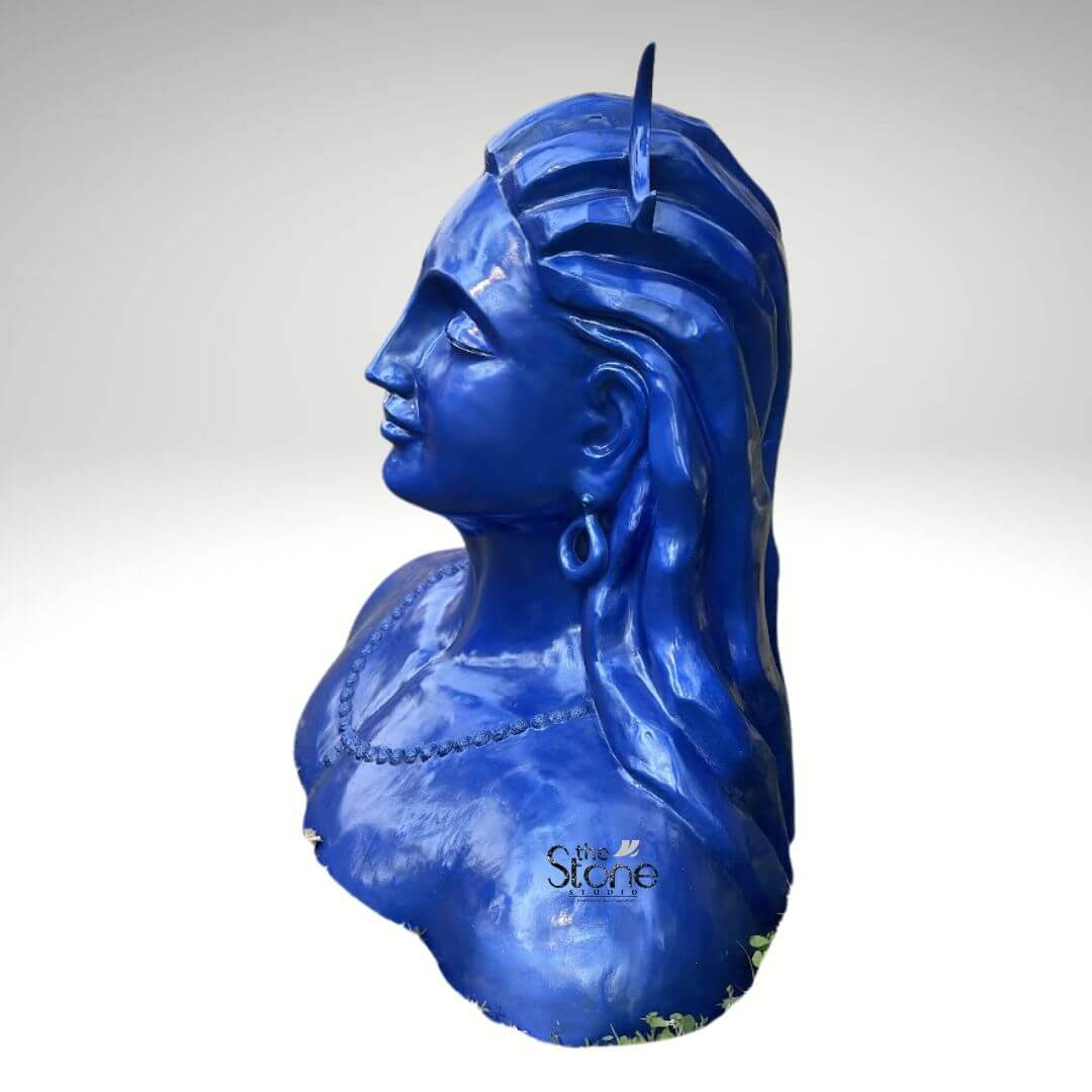 Blue Adiyogi Shiva Statue 4ft 4 A striking 4-foot fiber Adiyogi Shiva statue is presented from a side profile against a plain background making it an evocative piece for a yoga room. The sculpture captures the upper torso and head of Lord Shiva in his Adiyogi form depicted with closed eyes in deep meditation conveying profound inner peace and wisdom. His iconic third eye is subtly marked on his forehead and a crescent moon gracefully adorns his matted locks which are styled upwards and flow around his shoulders symbolizing his ascetic nature. The entire statue is rendered in a vibrant deep blue color characteristic of Shiva's divine complexion. Shiva's ear is adorned with a traditional large ring earring, visible on the side of his head. The intricate detailing on his hair and facial contours particularly the serene profile, showcases remarkable artistry. The smooth glossy finish of the fiber material enhances the statue's vibrant blue hue, making it a visually captivating piece that evokes both ancient reverence and modern artistic interpretation. The robust fiber construction ensures the statue is durable yet relatively lightweight, suitable for various indoor settings including a dedicated yoga room. While the full frontal view of his ornamentation is not visible the powerful silhouette and the dramatic flow of the hair combined with the tranquil facial expression contribute to the statue's commanding yet peaceful presence. A subtle hint of a beaded necklace is visible around his neck. This 4-foot fiber Adiyogi Shiva statue truly embodies spiritual power and artistic grace, with its intense blue color adding to its mystique. Its commanding yet tranquil presence makes it a powerful symbol of yoga and ultimate liberation perfect for inspiring meditation and focus in a yoga space.