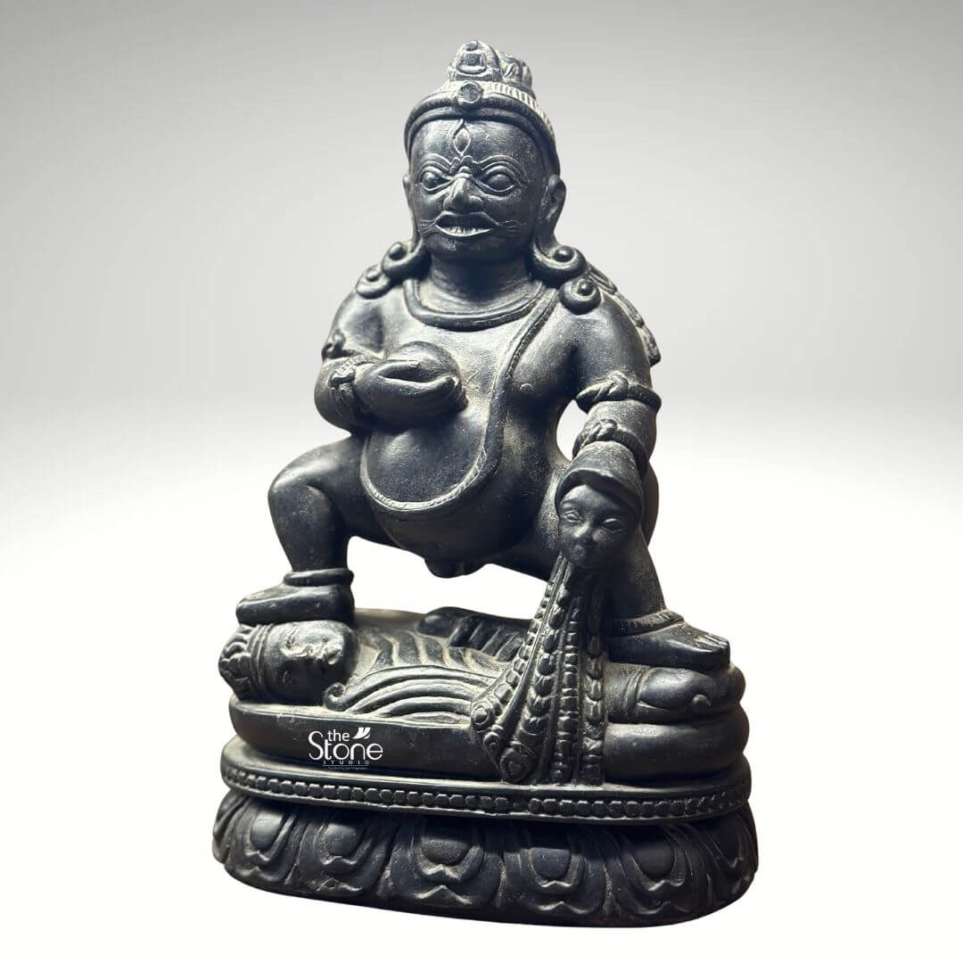 Black Stone Jambhala Statue 9" 2 A powerful 9-inch Jambhala statue carved from dark black stone stands out against a clean light-grey background emphasizing its robust form and intricate details. The deity is depicted in a commanding squatting posture radiating an aura of strength and determination. Jambhala's face is characterized by a stern yet benevolent expression with wide intense eyes and a prominent mustache conveying both his protective nature and his role as a bestower of wealth. The deep black stone exquisitely highlights the statue's muscular physique the folds of his belly and the rich textures of his adornments. Jambhala holds a small spherical jewel or fruit in his left hand a traditional symbol of abundance and prosperity. His right hand rests upon a mongoose which is shown expelling a stream of jewels a classic icon representing his power to generate wealth and alleviate poverty. The craftsmanship extends to the intricate details of his crown, earrings necklaces and armlets all rendered with precision in the dark stone. The statue rests on a beautifully carved double lotus pedestal a significant symbol in Buddhist iconography representing purity enlightenment and spiritual growth providing a grounding for the deity of material wealth. This image is ideally suited for an article focused on black Jambhala statues in stone showcasing a prime 9-inch example that embodies both spiritual significance and artistic mastery. The black stone material lends the statue a timeless and authoritative presence making it a compelling piece for a home office or shrine. The detailed depiction of Jambhala's attributes particularly the jewel-spitting mongoose directly communicates its connection to prosperity and protection making it a powerful visual for the article's discussion on this revered deity.
