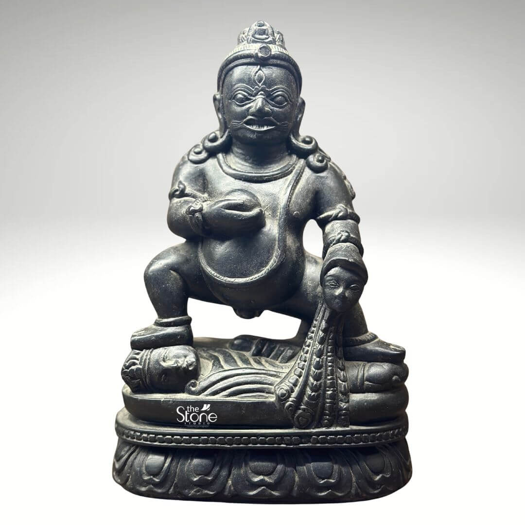 Black Stone Jambhala Statue 9" 1 A commanding 9-inch Jambhala statue meticulously carved from black stone is prominently displayed against a neutral background highlighting its intricate details and powerful presence. The deity is depicted in a squatting or crouching posture exuding a sense of robust strength and determination. Jambhala's facial features are distinct with a stern expression wide eyes and a slight smirk conveying both intensity and benevolence. The dark, polished black stone accentuates the statue's muscular form, the folds of his belly and the rich textures of his attire and ornamentation. Jambhala is shown holding a small round object in his left hand traditionally a jewel or fruit symbolizing wealth and prosperity. His right hand rests on a mongoose that is spewing jewels a classic attribute representing his ability to bestow riches and eliminate poverty. The detailed carving extends to his headdress armlets and necklace all intricately rendered in the black stone. The statue rests on a beautifully sculpted lotus pedestal a common motif in Buddhist and Hindu iconography symbolizing purity and spiritual awakening despite being associated with material wealth. This image is ideally suited for an article discussing black stone Jambhala statues showcasing a prime example for collectors or those seeking symbols of prosperity for their homes or altars. The 9-inch size makes it a significant yet manageable piece and the black stone material lends it a timeless imposing quality. The detailed depiction of Jambhala's attributes and powerful posture directly conveys its connection to wealth protection, and spiritual abundance making it a compelling subject for the article's focus.