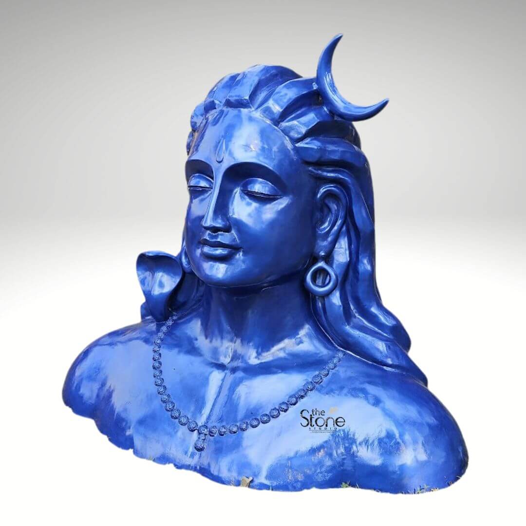 Blue Adiyogi Shiva Statue 4ft 5 A striking 4-foot fiber statue of the Blue Adiyogi Shiva bust is prominently displayed against a plain background making it an evocative piece for a garden. The sculpture captures the upper torso and head of Lord Shiva in his Adiyogi form depicted with closed eyes in deep meditation conveying profound inner peace and wisdom. His iconic third eye is subtly marked on his forehead and a prominent crescent moon gracefully adorns his matted locks which are styled upwards and flow around his shoulders symbolizing his ascetic nature. The entire statue is rendered in a vibrant deep blue color characteristic of Shiva's divine complexion which would create a captivating contrast with natural greenery. Shiva's ears are adorned with traditional large ring earrings and a detailed serpent is carved around his neck, along with a beaded necklace adding to his divine iconography. The intricate detailing on his hair, ornaments and facial features showcases remarkable artistry. The smooth glossy finish of the fiber material enhances the statue's vibrant blue hue making it a visually captivating piece that evokes both ancient reverence and modern artistic interpretation. The robust fiber construction ensures the statue is durable and weather-resistant perfectly suited for outdoor display in a garden setting. The statue's bust-like form with its broad shoulders and serene countenance exudes a powerful yet tranquil presence making it a compelling focal point in any garden. This 4-foot fiber Blue Adiyogi Shiva statue truly embodies spiritual power and artistic grace with its intense blue color adding to its mystique. Its commanding yet peaceful presence makes it a powerful symbol of yoga and ultimate liberation perfect for inspiring contemplation and reverence within an outdoor sanctuary.