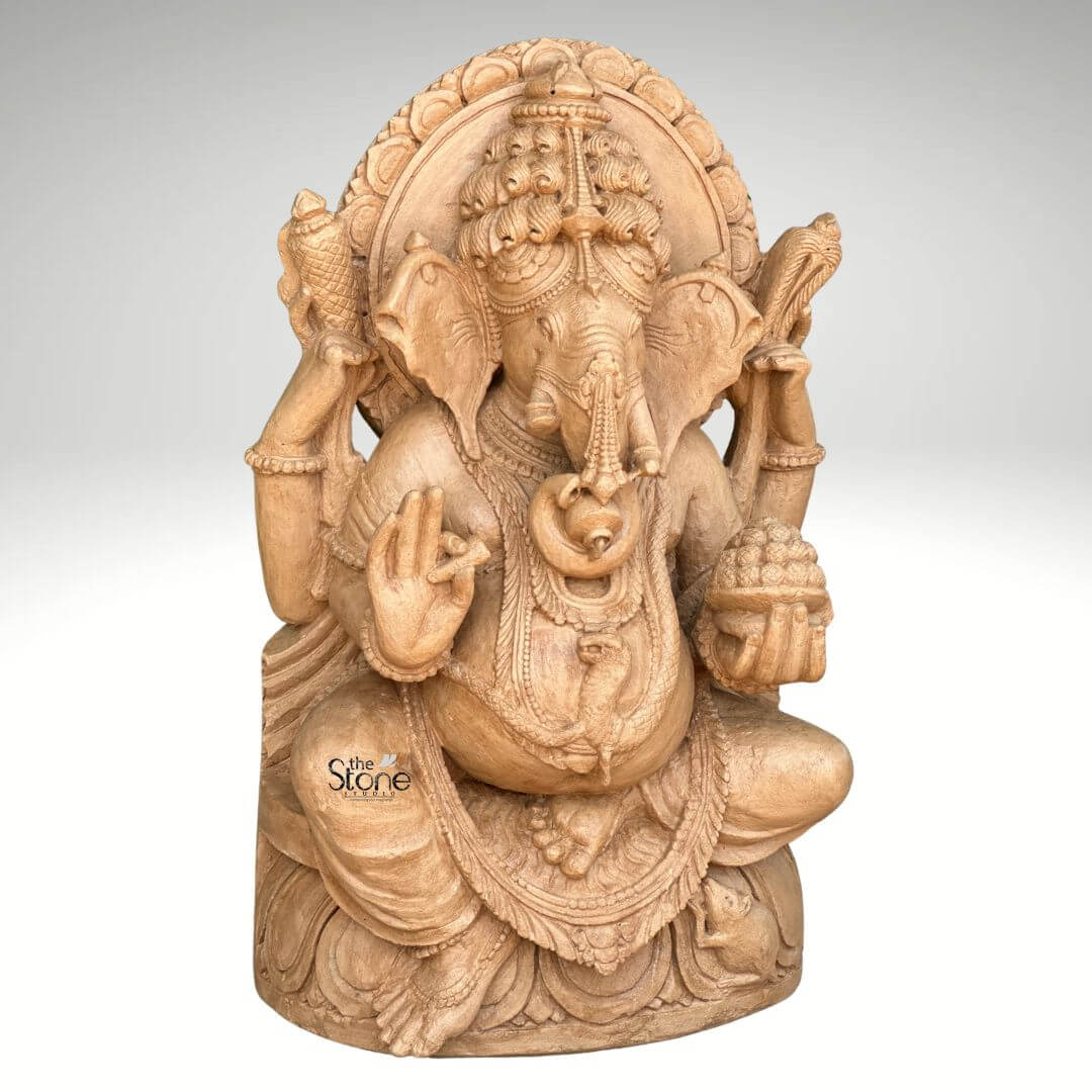 3ft Sitting Ganesha Statue 5 A magnificent 3-foot brown sandstone Ganesh statue is prominently displayed against a plain background making it a captivating subject for an article about such sculptures. Lord Ganesha is depicted in a traditional seated posture with his iconic elephant head adorned by an elaborate crown and intricate carvings detailing his large ears and trunk. He is shown with four arms holding a conch shell and an axe in his upper hands a modak in one lower hand and his other lower hand raised in a gesture of blessing symbolizing protection and grace. The statue is richly adorned with necklaces armlets and a sacred thread draped across his plump belly all meticulously carved from the brown sandstone. The large ears and expressive eyes give the Ganesha statue a benevolent and wise demeanor. Behind his head a circular halo like structure is intricately carved with traditional patterns further accentuating his divine aura. The craftsmanship is evident in every detail from the delicate folds of his dhoti to the robust and powerful rendering of his form all enhanced by the warm natural hue and textured finish of the brown sandstone. Ganesha is seated on a lotus pedestal which is also intricately carved with floral motifs and drapery providing a stable and aesthetically pleasing foundation. The brown sandstone's natural characteristics highlight the deep textures and intricate patterns of the carving, making every detail stand out with an ancient and earthy feel. This 3-foot brown sandstone Ganesh statue truly embodies spiritual reverence and artistic excellence serving as a powerful and beautiful representation of the beloved deity.