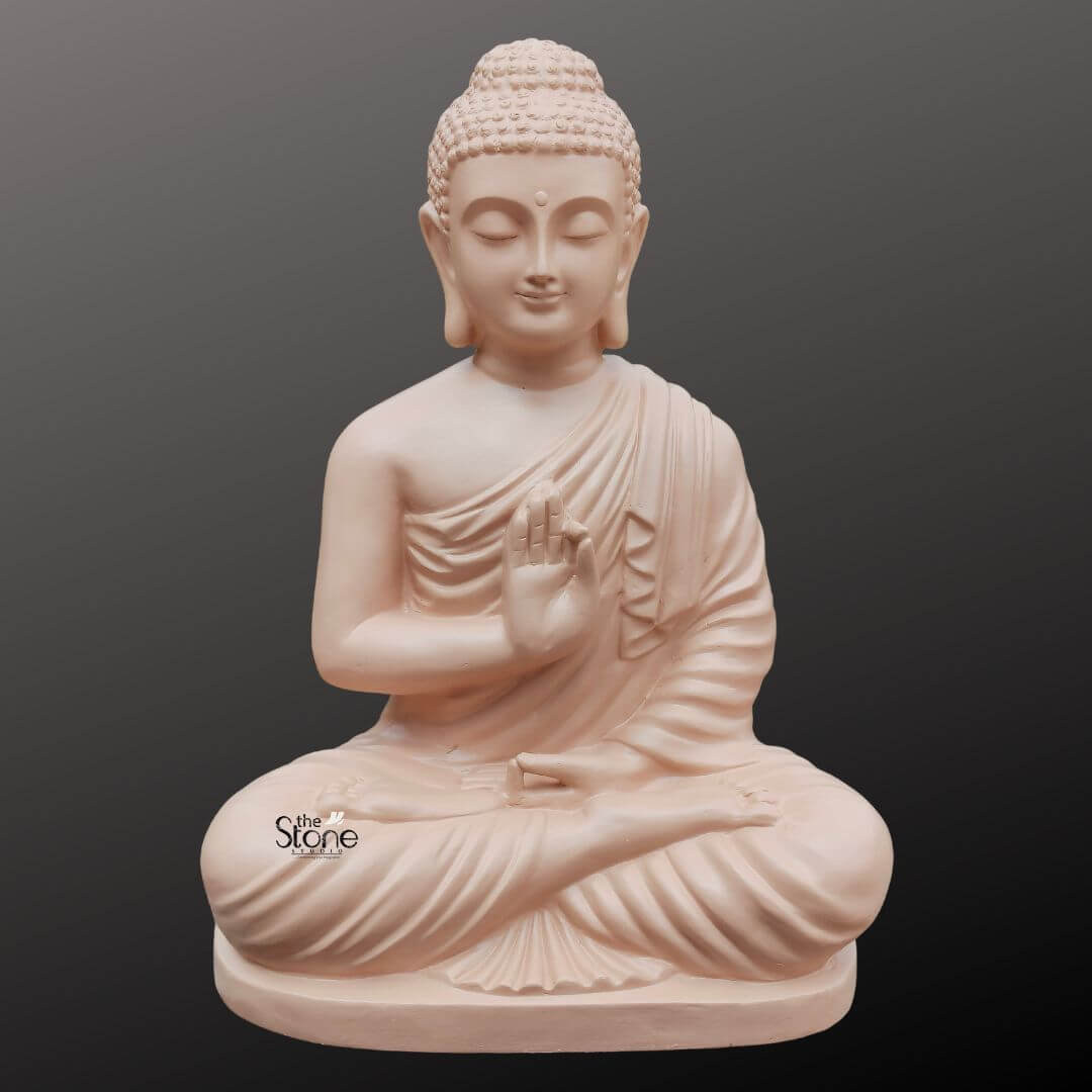 Buddha Statue for Zen Decor 2ft 1 A serene 2-foot fiber Buddha statue with a smooth light beige finish is elegantly presented against a dark gradient background making it an ideal piece for Zen decor. The Buddha is depicted in the Vitarka Mudra with his right hand raised palm outward and thumb and index finger touching to form a circle symbolizing the teaching and transmission of Buddhist doctrines. His left hand rests gently in his lap palms upward. Seated in full lotus position his eyes are gently closed conveying profound inner peace and spiritual wisdom while a subtle smile graces his lips and his elongated earlobes are visible all characteristic features of traditional Buddha iconography. The detailing on the statue is meticulously rendered from the individual curls of his hair gathered in a prominent topknot to the graceful natural folds of his monastic robe that drape softly over his left shoulder and body. The smooth matte finish of the fiber material gives the statue a natural stone-like appearance perfectly aligning with the minimalist and organic aesthetics of Zen decor. The light beige color evokes a sense of calm and purity enhancing its contemplative presence. The fiber construction ensures that the statue is robust yet lighter than traditional stone offering both aesthetic appeal and practical versatility for various settings. The Buddha statue rests on a simple low and subtly curved rectangular base which seamlessly integrates with the overall form providing stability without distracting from the main figure. This 2-foot fiber Buddha statue with its elegant finish and peaceful demeanor embodies tranquility and spiritual grace serving as a captivating subject for an article exploring aesthetically pleasing and durable Buddha statues suitable for enhancing the serene and meditative ambiance of Zen-inspired home decor.