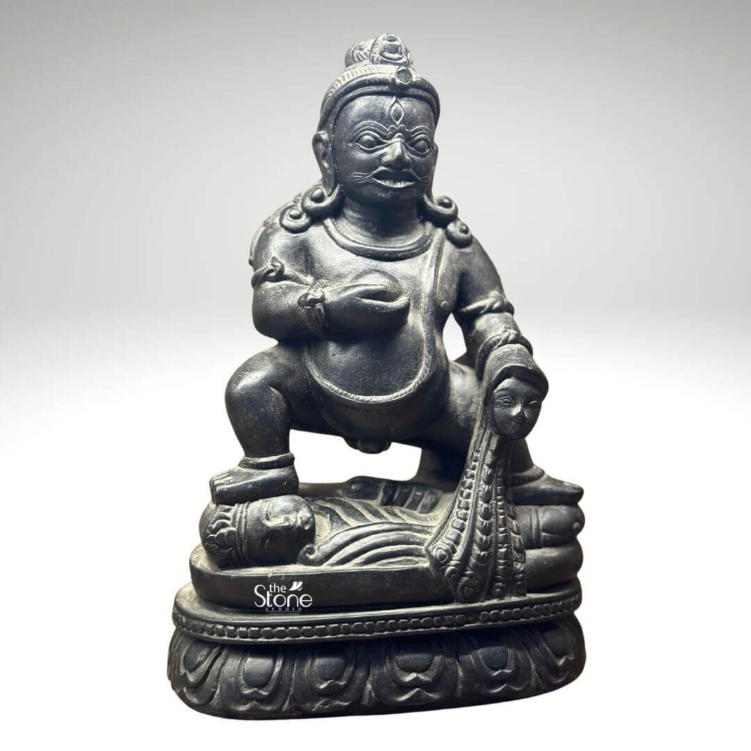 Black Stone Jambhala Statue 9" 4 A striking 9-inch Buddhist Jambhala statue masterfully carved from black stone is presented against a clean light-grey background allowing its intricate details and powerful form to take center stage. The deity is depicted in a dynamic squatting posture conveying an aura of strength protection and generosity. Jambhala's facial expression is a compelling mix of fierceness and benevolence characterized by wide, intense eyes a prominent mustache and a slight smirk symbolizing his role as a guardian of wealth and dispeller of poverty. The deep black stone exquisitely captures the statue's muscular physique and the rich textures of his attire and ornamentation. In his left hand Jambhala holds a spherical object traditionally identified as a jewel or a fruit representing the bestowal of riches and spiritual abundance. His right hand rests upon a stylized mongoose a significant attribute in Buddhist iconography shown gracefully expelling a cascade of jewels symbolizing his power to grant material wealth. The craftsmanship extends to the intricate details of his crown, earrings necklaces and armlets all precisely rendered in the dark stone. The statue is seated on a beautifully sculpted lotus pedestal a profound symbol of purity enlightenmen and spiritual growth in Buddhism even for a deity associated with earthly prosperity. This image is exceptionally well-suited for an article focused on Buddhist Jambhala statues showcasing a prime 9-inch black stone example that embodies both spiritual significance and artistic mastery. The black stone material gives the statue a timeless and authoritative presence making it a compelling piece for a home altar meditation space or personal collection. The detailed depiction of Jambhala's attributes particularly the jewel-spitting mongoose directly communicates his benevolent function in Buddhist practice making this a powerful visual for the article's discussion on this revered deity of wealth and prosperity.