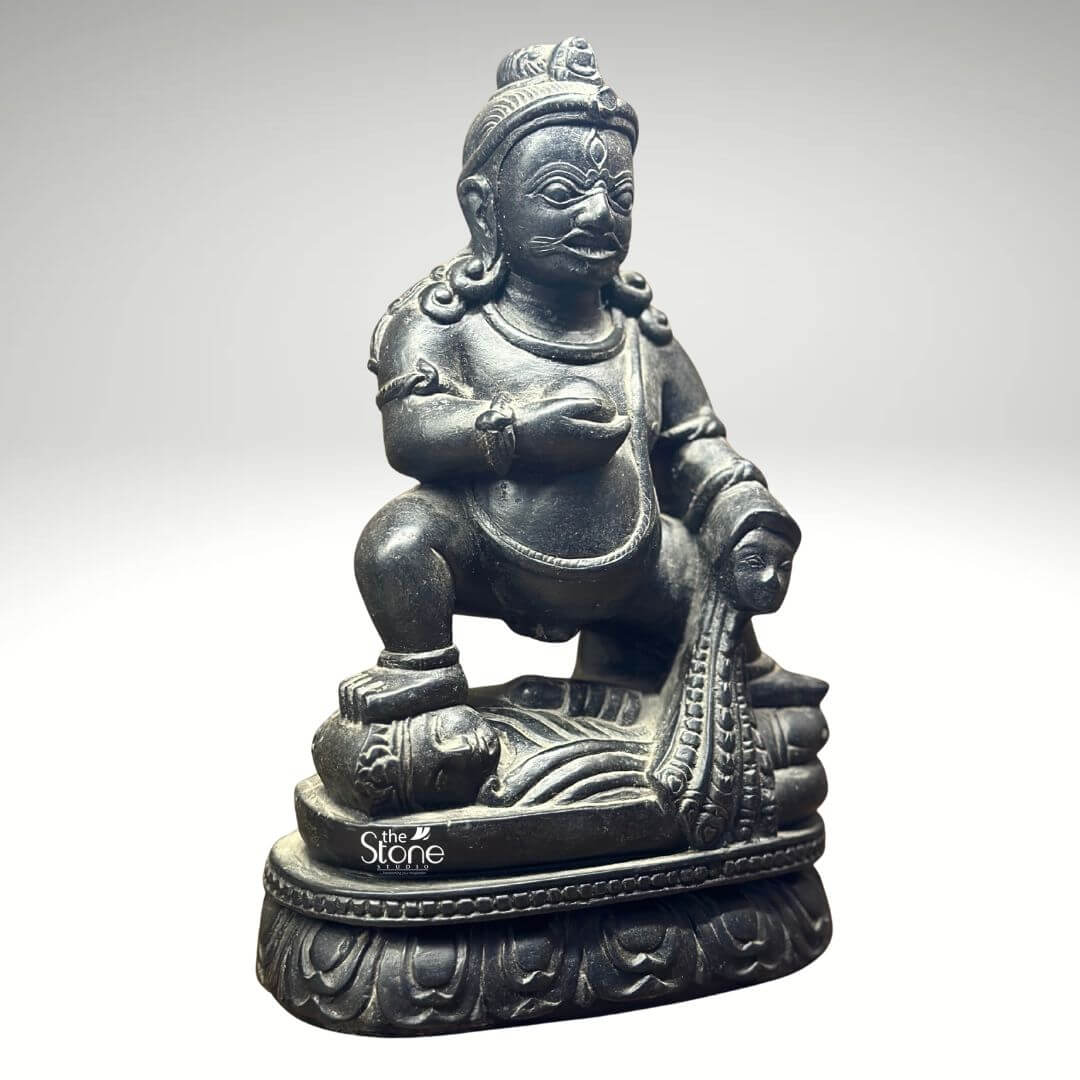 Black Stone Jambhala Statue 9" 5 A commanding 9-inch Dzambhala statue meticulously carved from black stone is prominently displayed against a neutral background highlighting its intricate details and powerful presence. The deity is depicted in a dynamic squatting posture exuding an aura of robust strength protection and generosity. Dzambhala's facial features are distinct with wide intense eyes a prominent mustache and a stern yet benevolent expression conveying his role as a guardian of wealth and dispeller of poverty. The deep polished black stone exquisitely captures the statue's muscular physique the folds of his belly and the rich textures of his attire and ornamentation. In his left hand Dzambhala holds a spherical object traditionally identified as a jewel or a fruit representing the bestowal of riches and spiritual abundance. His right hand rests upon a stylized mongoose a significant attribute in Buddhist iconography shown gracefully expelling a cascade of jewels symbolizing his power to grant material wealth. The craftsmanship extends to the intricate details of his crown, earrings necklaces and armlets all precisely rendered in the dark stone. The statue is seated on a beautifully sculpted lotus pedestal a profound symbol of purity enlightenment and spiritual growth providing a sacred foundation for the deity of material prosperity. This image is ideally suited for an article focused on Dzambhala statues for home temples showcasing a prime 9-inch black stone example that embodies both spiritual significance and artistic mastery. The black stone material gives the statue a timeless and authoritative presence making it a compelling piece for a home altar meditation space or personal collection. The detailed depiction of Dzambhala's attributes particularly the jewel-spitting mongoose directly communicates his benevolent function in Buddhist practice making this a powerful visual for the article's discussion on this revered deity of wealth and prosperity perfect for enhancing the spiritual ambiance of a home temple.