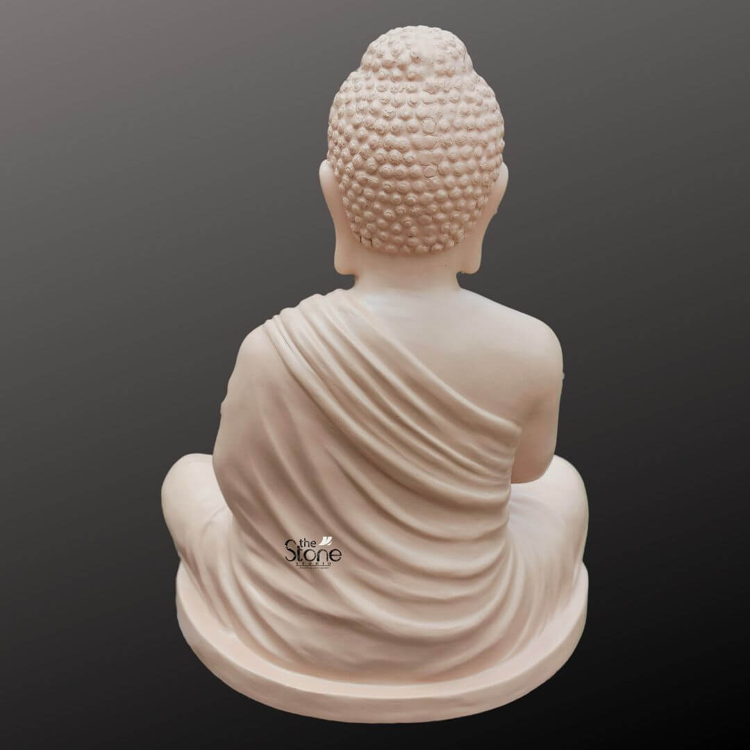 Buddha Statue for Zen Decor 2ft 5 A serene 2-foot fiber Buddha statue with a smooth light beige finish is gracefully presented from a rear view against a dark gradient background making it an ideal piece for home decor. The Buddha is depicted in a meditative pose seated in full lotus position with his hands resting gently in his lap symbolizing deep contemplation and enlightenment. From this perspective the prominent tightly curled hair gathered in a topknot is clearly visible along with the dignified posture of his head and back conveying profound inner peace and spiritual wisdom. The smooth matte finish of the fiber material gives the statue a natural stone-like appearance. The detailing on the idol is meticulously rendered with particular emphasis on the graceful natural folds of his monastic robe that drape softly over his back and shoulders extending down to his crossed legs. The light plays across the contours of the statue highlighting the subtle texture of the robe and the smooth surface of the fiber creating gentle shadows that add depth to the form. The light beige color evokes a sense of calm and purity enhancing its contemplative presence. The fiber construction ensures that the statue is robust yet lighter than traditional stone, offering both aesthetic appeal and practical versatility for various home decor settings. The Buddha idol rests on a simple, low and subtly curved rectangular base which seamlessly integrates with the overall form providing stability without distracting from the main figure. This 2-foot fiber Buddha statue with its elegant finish and peaceful demeanor embodies tranquility and spiritual grace serving as a compelling subject for an article exploring aesthetically pleasing and durable Buddha statues suitable for enhancing the serene ambiance of any home.