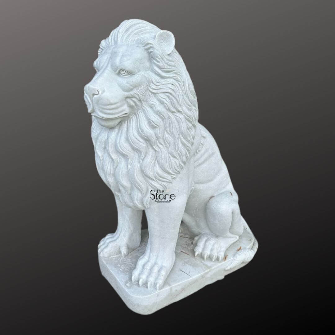 White Marble Lion Statue 5ft 2 A magnificent handcrafted marble lion statue is prominently displayed from a slight side angle against a dark gradient background embodying strength and regal elegance. The lion is meticulously sculpted in a seated position with its front paws extended forward and its powerful body held upright. Its head is turned to the left featuring a detailed fierce yet noble expression with deep-set eyes and a strong muzzle. The intricate carving highlights the textured flowing mane which cascades around its head and shoulders giving it a voluminous and majestic appearance. The statue is crafted from pristine white marble which beautifully emphasizes the fine details of the carving from the individual strands within the mane to the sharp claws on its paws. The smooth polished surface of the marble subtly reflects light accentuating the contours and musculature of the lion's form. The natural beauty and purity of the marble are showcased underlining the artisan's skill in transforming raw stone into such a lifelike and commanding figure. The handcrafted marble lion statue rests on a sturdy rectangular base also carved from matching white marble providing a solid foundation and integrating seamlessly with the overall design. This elegant sculpture captures the essence of a powerful guardian and a symbol of royalty making it a captivating subject for an article exploring handcrafted marble lion statues their symbolism and their use in grand architectural or decorative settings.