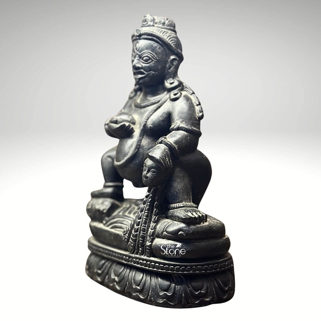 Black Stone Jambhala Statue 9" 7 A commanding 9-inch Jambhala idol meticulously carved from black stone is presented at a slight angle against a clean light-grey background highlighting its robust form and intricate details. The deity is depicted in a dynamic squatting posture exuding an aura of powerful strength protection and generosity. Jambhala's facial features are distinct with wide intense eyes a prominent mustache and a stern yet benevolent expression conveying his role as a guardian of wealth and dispeller of poverty. The deep polished black stone exquisitely captures the statue's muscular physique the folds of his belly and the rich textures of his attire and ornamentation. In his left hand Jambhala holds a spherical object traditionally identified as a jewel or a fruit representing the bestowal of riches and spiritual abundance. His right hand rests upon a stylized mongoose a significant attribute in Buddhist iconography shown gracefully expelling a cascade of jewels symbolizing his power to grant material wealth. The craftsmanship extends to the intricate details of his crown, earrings necklaces and armlets all precisely rendered in the dark stone. The statue is seated on a beautifully sculpted lotus pedestal a profound symbol of purity enlightenment and spiritual growth providing a sacred foundation for the deity of material prosperity. This image is ideally suited for an article focused on Jambhala idols for prosperity showcasing a prime 9-inch black stone example that embodies both spiritual significance and artistic mastery. The black stone material gives the idol a timeless and authoritative presence making it a compelling piece for a home altar office or personal collection where the intention is to invite good fortune and abundance. The detailed depiction of Jambhala's attributes particularly the jewel-spitting mongoose directly communicates his benevolent function in Buddhist practice making this a powerful visual for the article's discussion on this revered deity of wealth and prosperity.