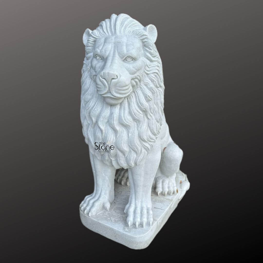 White Marble Lion Statue 5ft 5 A majestic marble lion sculpture is prominently displayed against a dark gradient background embodying strength and regal elegance perfect for a garden setting. The lion is sculpted in a seated position with its front paws extended forward and its powerful body held upright. Its head is turned slightly featuring a detailed fierce yet noble expression with deep-set eyes and a strong muzzle giving it a watchful demeanor suitable for a garden guardian. The intricate carving brilliantly highlights the texture of its voluminous flowing mane which cascades around its head and shoulders conveying a sense of immense power and majesty. The sculpture is crafted from pristine white marble which exquisitely emphasizes the fine details of the carving from the individual strands within the mane to the sharp claws on its paws. The smooth polished surface of the marble subtly reflects light accentuating the contours and musculature of the lion's formidable form. The natural beauty and purity of the marble are showcased underlining the artisan's skill in transforming raw stone into such a lifelike and commanding figure that would stand out gracefully amidst greenery. The marble lion sculpture rests on a sturdy rectangular base also carved from matching white marble providing a solid foundation that integrates seamlessly with the overall design. This elegant sculpture captures the essence of a powerful guardian and a timeless symbol of royalty and strength making it a captivating subject for an article exploring marble lion sculptures and their commanding presence when used for garden decor.