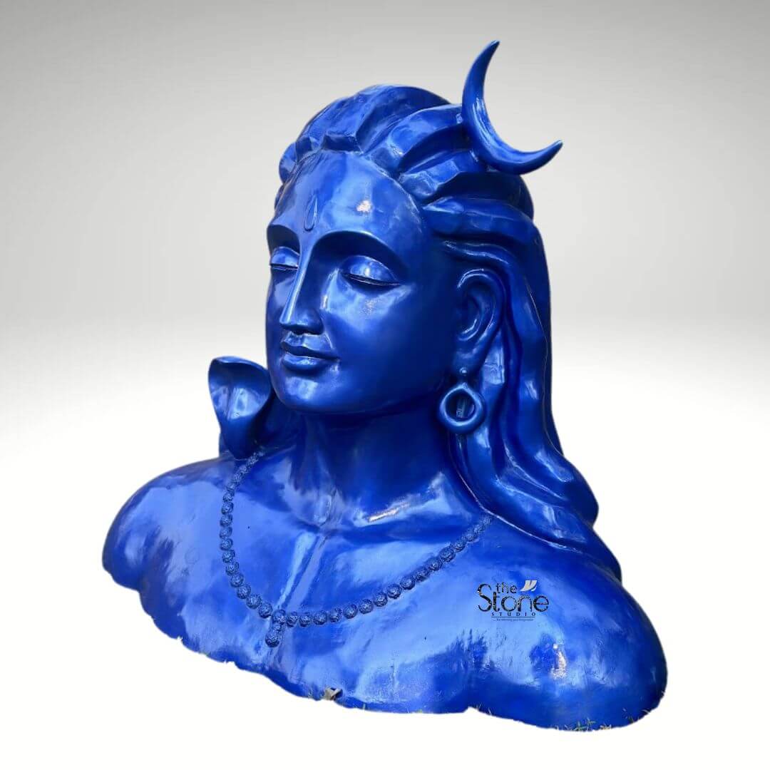 Blue Adiyogi Shiva Statue 4ft 10 A striking 4-foot fiber Shiva bust statue, with a vibrant blue finish is prominently displayed against a plain background making it an evocative piece for an article about such sculptures. The sculpture captures the upper torso and head of Lord Shiva in his Adiyogi form depicted with closed eyes in deep meditation conveying profound inner peace and wisdom. His iconic third eye is subtly marked on his forehead and a prominent crescent moon gracefully adorns his matted locks which are styled upwards and flow around his shoulders symbolizing his ascetic nature. The entire statue is rendered in a vibrant deep blue color characteristic of Shiva's divine complexion. Shiva's ears are adorned with traditional large ring earrings and a detailed serpent is subtly carved around his neck, along with a beaded necklace adding to his divine iconography. The intricate detailing on his hair, ornaments and facial features showcases remarkable artistry. The smooth, glossy finish of the fiber material enhances the statue's vibrant blue hue, making it a visually captivating piece that evokes both ancient reverence and modern artistic interpretation. The robust fiber construction ensures the statue is durable yet relatively lightweight suitable for various indoor and outdoor settings. The statue's bust-like form, with its broad shoulders and serene countenance exudes a powerful yet tranquil presence making it a compelling focal point. This 4-foot fiber Shiva bust statue, with its intense blue finish truly embodies spiritual power and artistic grace. Its commanding yet peaceful presence makes it a powerful symbol of yoga and ultimate liberation perfect for inspiring contemplation and reverence.