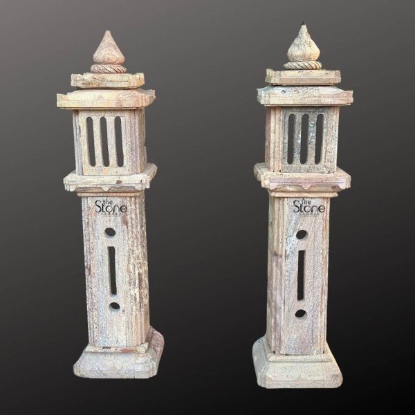 A striking pair of 4-foot stone garden lamps crafted from brown sandstone stands prominently against a dark neutral background emphasizing their rustic charm and architectural details. Each lamp is designed as a tall slender column with a square base tapering upwards to a traditional lantern-style top. The brown sandstone with its visible grain and subtle variations in tone gives the lamps a weathered aged appearance highlighting their natural material and traditional craftsmanship. Each lamp features a multi-tiered structure with the main body presenting a solid rectangular pillar. The upper section of each lamp resembles a pagoda-style lantern complete with vertical slats for light to escape and a tiered roof culminating in a pointed finial. The weathered texture and natural imperfections of the sandstone are evident across the entire surface adding to their authentic antique appeal. Small circular cutouts are visible on the lower pillar section possibly for additional light diffusion or decorative purposes. The design suggests inspiration from traditional Japanese or East Asian stone lanterns often found in Zen gardens. This image is ideally suited for an article discussing stone garden lamp pairs showcasing these 4-foot brown sandstone pieces as elegant and functional additions to outdoor spaces. Their substantial height makes them suitable for lining pathways accentuating garden features or marking an entryway. The durable sandstone ensures their longevity and aesthetic appeal in various weather conditions. The traditional design and natural material directly convey a sense of serenity and timelessness making them perfect for enhancing the ambiance of a garden inviting a peaceful and contemplative atmosphere with their soft diffused light.