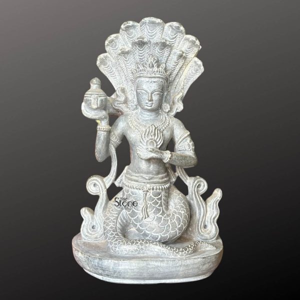 A captivating 6-inch Naga Kanya statue meticulously carved from green stone is presented against a dark neutral background emphasizing its intricate details and mythical grace. The deity is depicted in a seated posture with the lower half of her body taking the form of a coiled serpent showcasing intricate scales. The upper half is human adorned with a crown and traditional jewelry. The greenish hue of the stone with its subtle variations gives the statue a natural weathered appearance highlighting its traditional craftsmanship and organic beauty. A prominent feature of the Naga Kanya is the magnificent multi-headed cobra hood that rises majestically behind her human upper body fanning out in an impressive display of divine protection and power. In her hands she holds symbolic objects one hand delicately grasps a small pot or vessel traditionally associated with abundance or elixir while the other holds a flaming object possibly representing light or spiritual energy. Her face is serene and benevolent with finely sculpted features and an ornate crown conveying a sense of ancient wisdom and mystical charm. The base of the statue is adorned with wavy patterns suggesting water or the undulating movement of a serpent. This image is ideally suited for an article discussing stone Naga Kanya statues underscoring their significance in various Asian mythologies as protectors of water bodies and guardians of treasure. The 6-inch size makes it a versatile piece for placement in home temples gardens or as a unique decorative item. The durable green stone ensures its longevity and aesthetic appeal. The detailed depiction of the serpent body cobra hood, and symbolic attributes directly conveys its mystical connection and benevolent protective qualities making it a compelling subject for the article's focus on this revered mythical being.