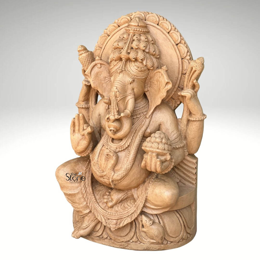 3ft Sitting Ganesha Statue 6 A magnificent 3-foot brown sandstone Ganesha statue is prominently displayed against a plain background making it an ideal Traditional Ganpati Murti for Home. Lord Ganesha is depicted in a traditional seated posture with his iconic elephant head adorned by an elaborate crown and intricate carvings detailing his large ears and trunk. He is shown with four arms holding a conch shell and an axe in his upper hands a modak in one lower hand and his other lower hand raised in a gesture of blessing symbolizing protection and grace for the home. The statue is richly adorned with necklaces armlets and a sacred thread draped across his plump belly all meticulously carved from the brown sandstone. The large ears and expressive eyes give the Ganesha statue a benevolent and wise demeanor. Behind his head a circular halo-like structure is intricately carved with traditional patterns further accentuating his divine aura and spiritual presence. The craftsmanship is evident in every detail from the delicate folds of his dhoti to the robust and powerful rendering of his form all enhanced by the warm natural hue and textured finish of the brown sandstone. Ganesha is seated on a lotus pedestal which is also intricately carved with floral motifs and drapery providing a stable and aesthetically pleasing foundation. The brown sandstone's natural characteristics highlight the deep textures and intricate patterns of the carving making every detail stand out with an ancient and earthy feel. This 3-foot brown sandstone Ganesha statue truly embodies spiritual reverence and artistic excellence serving as a powerful and beautiful representation of the beloved deity perfect for a traditional home setting.
