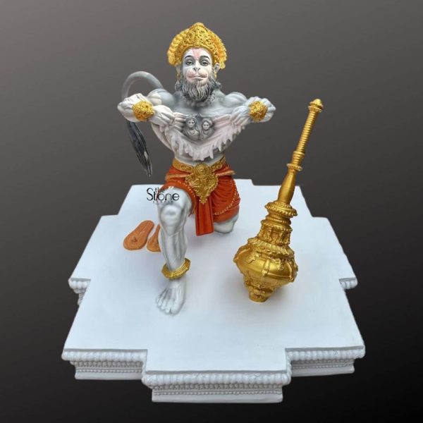 A vibrant fiber Veer Hanuman statue is dynamically posed on a white stepped base capturing the powerful essence of the revered deity. Hanuman is depicted in a kneeling stance with one knee on the ground and the other leg bent showcasing his incredible strength and devotion. His chest is dramatically torn open revealing miniature figures of Lord Rama and Sita within his heart, a classic iconographic representation of his unwavering loyalty. Hanuman's body is predominantly light gray suggesting his divine robust form with his face featuring a nuanced expression that combines determination with reverence highlighted by his white beard and mustache and subtle pinkish tones around his mouth. He is adorned with rich golden ornaments including a magnificent crown armbands wristbands and anklets which contrast beautifully with his gray skin. A bright orange dhoti is draped around his waist secured by an ornate golden belt adding a splash of color and royal dignity to his attire. His tail a significant attribute is visible arching behind him ark and powerful. To his right a large intricately detailed golden mace a symbol of his immense power and protection rests on the base completing his iconic representation. The Gada itself is highly decorative featuring multiple tiers and elaborate carvings. The statue rests on a multi-tiered white base with carved architectural details suggesting a pedestal suitable for worship or prominent display. The background is a simple, dark gray gradient ensuring that all attention remains on the colorful and detailed statue. This image effectively illustrates an article about Veer Hanuman statues particularly those crafted from fiber emphasizing his strength, devotion and the iconic narrative of his loyalty to Rama and Sita, making it a compelling piece for devotees and collectors alike.