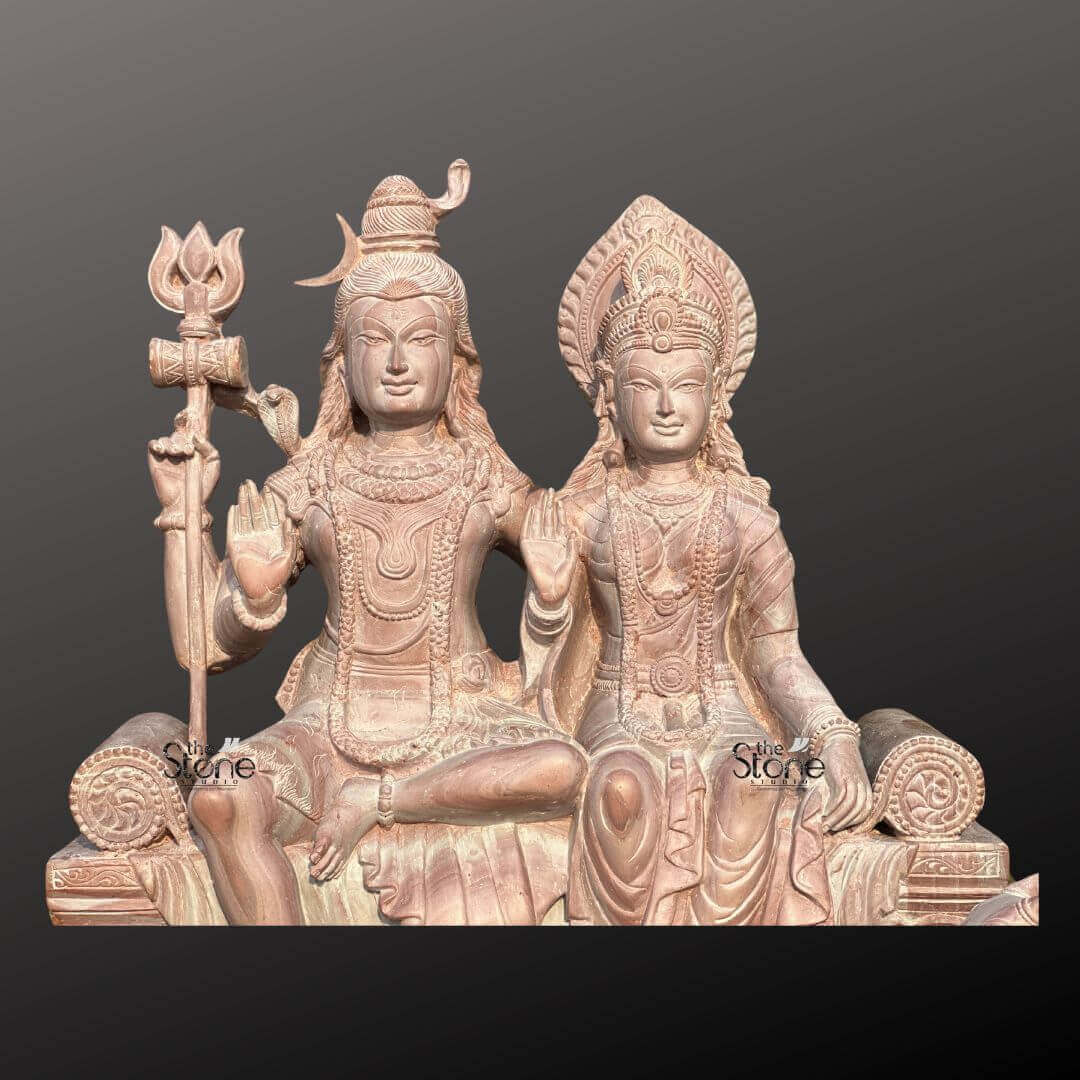 Lord Siva with Maa Parvati Stone Statue 18" 2 An exquisite 18-inch Shiva Parvati Sculpture meticulously carved from pink stone presented against a dark background as highlighted in an article about such sculptures. The entire piece rendered in a soft warm pinkish-brown hue of natural stone exudes a gentle and serene aesthetic. Lord Shiva and Goddess Parvati are depicted seated side-by-side on an ornate throne. Lord Shiva on the left is depicted with his traditional matted hair adorned with a crescent moon and a small cobra. He holds a trishul in his left hand while his right hand is raised in the Abhaya Mudra. He wears minimal attire and intricate jewelry all carved from the stone. Goddess Parvati sits gracefully to Shiva's right adorned with an elaborate crown and traditional jewelry including necklaces and earrings. Her right hand is also raised in a blessing gesture while her left hand rests elegantly in her lap. Both deities have serene expressions conveying peace and divine harmony. The throne they share is intricately carved with traditional Indian motifs including a lion's face at the front symbolizing strength and royalty. The flowing drapery of their garments is also finely sculpture adding a sense of detail and elegance. The statue rests on a robust and ornate base also crafted from pink stone featuring lotus petal designs and other decorative patterns. The smooth contours and fine details throughout both figures emphasize a deep sense of tranquility and spiritual harmony. This 18-inch Shiva Parvati sculpture in its unique pink stone is a powerful representation of devotion and artistic mastery making it an ideal piece for spiritual veneration and artistic appreciation in a home or temple as discussed in the accompanying article.