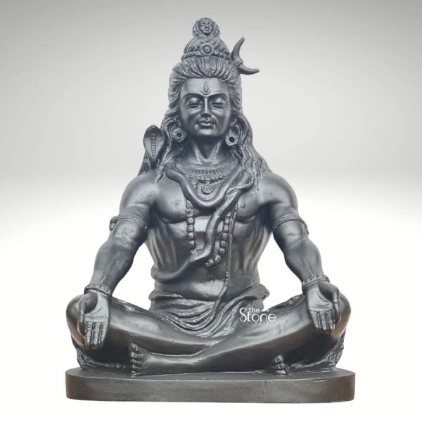A powerful 2 Feet Black Granite Meditating Lord Shiva Statue meticulously carved from dark blackstone is presented against a clean light background highlighting its serene yet commanding presence. This 2 Feet Blackstone Shiva Statue depicts Lord Shiva in a deep meditative state seated in the traditional cross-legged lotus position. His eyes are gently closed conveying profound inner peace and unwavering spiritual focus perfectly capturing the essence of a Black Granite Meditating Lord Shiva Statue. The smooth polished surface of the blackstone gleams accentuating the well-defined musculature of his physique and the intricate details of his divine attributes. Lord Shiva is adorned with his iconic symbols: his hair is styled in a jatamukuta on top of his head from which the crescent moon and the Ganges river emerge. A prominent cobra is coiled around his neck and shoulders serving as his sacred adornment. His third eye is subtly marked on his forehead. He wears minimal jewelry including beaded necklaces and armbands, emphasizing his ascetic nature. His hands rest in his lap in a meditative mudra further reinforcing his state of profound concentration. The striking black granite finish of the stone adds a sense of timeless majesty and solemnity. The statue rests on a solid rectangular blackstone base providing a sturdy and dignified foundation. The intricate carving of his dhoti shows subtle fods adding texture and realism to the figure. The overall composition of this 2 Feet Blackstone Shiva Statue powerfully conveys Lord Shivas immense spiritual power divine tranquility and ascetic wisdom. This detailed description effectively connects the visual elements of the blackstone sculpture with its Black Granite appearance and its spiritual significance making it an ideal representation for an article about a Black Granite Meditating Lord Shiva Statue.